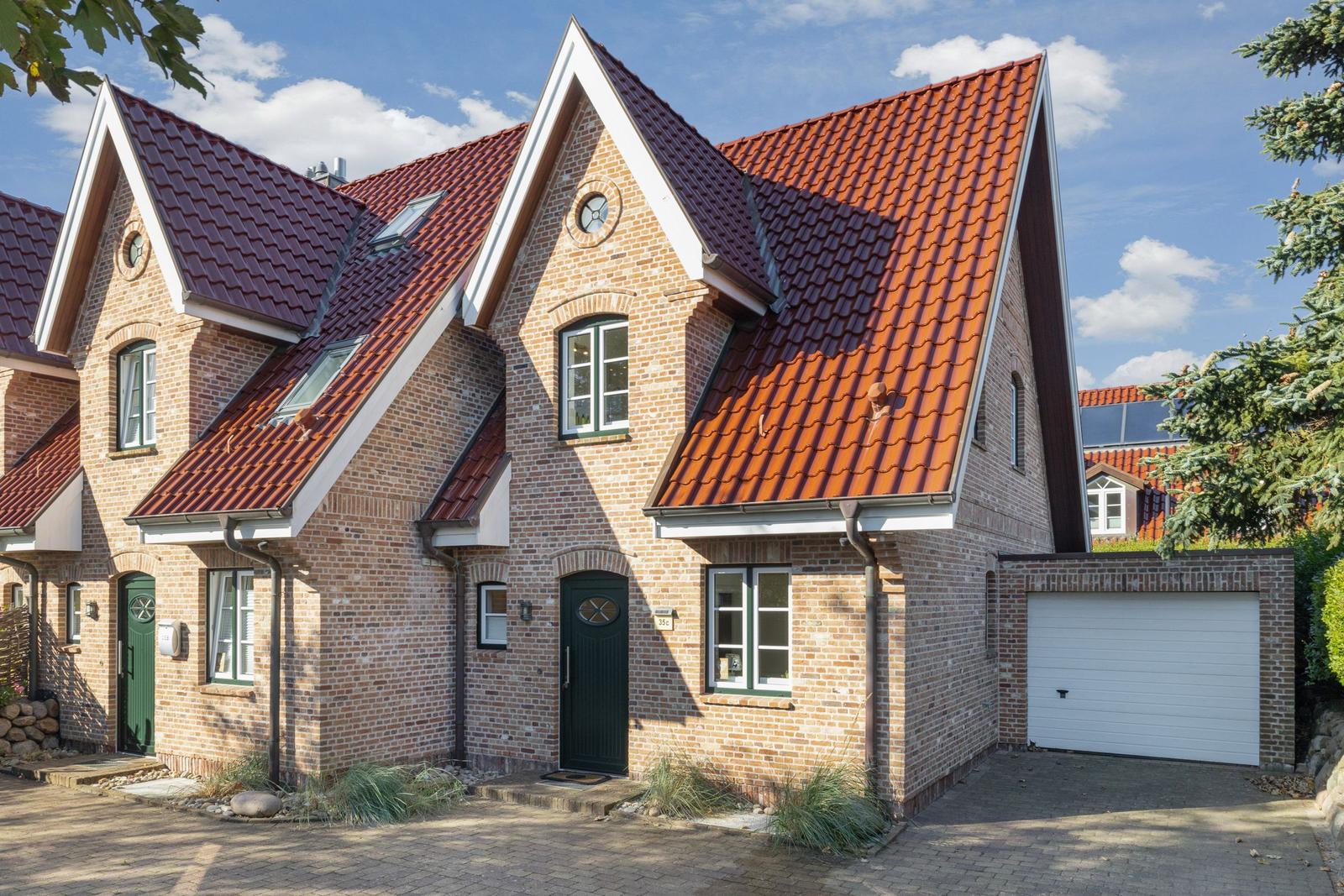 House with red tiled roof and brick facade, green doors and white garage door.