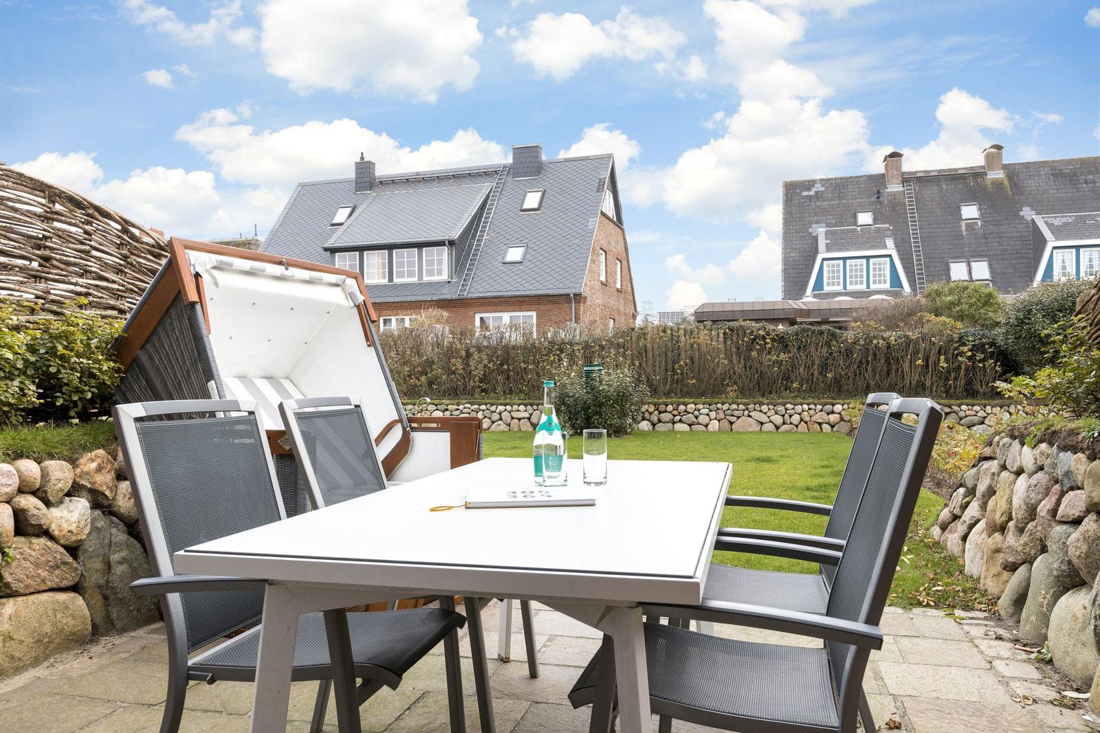 Terrace with table, chairs, and sunshade. Green areas and houses in the background.