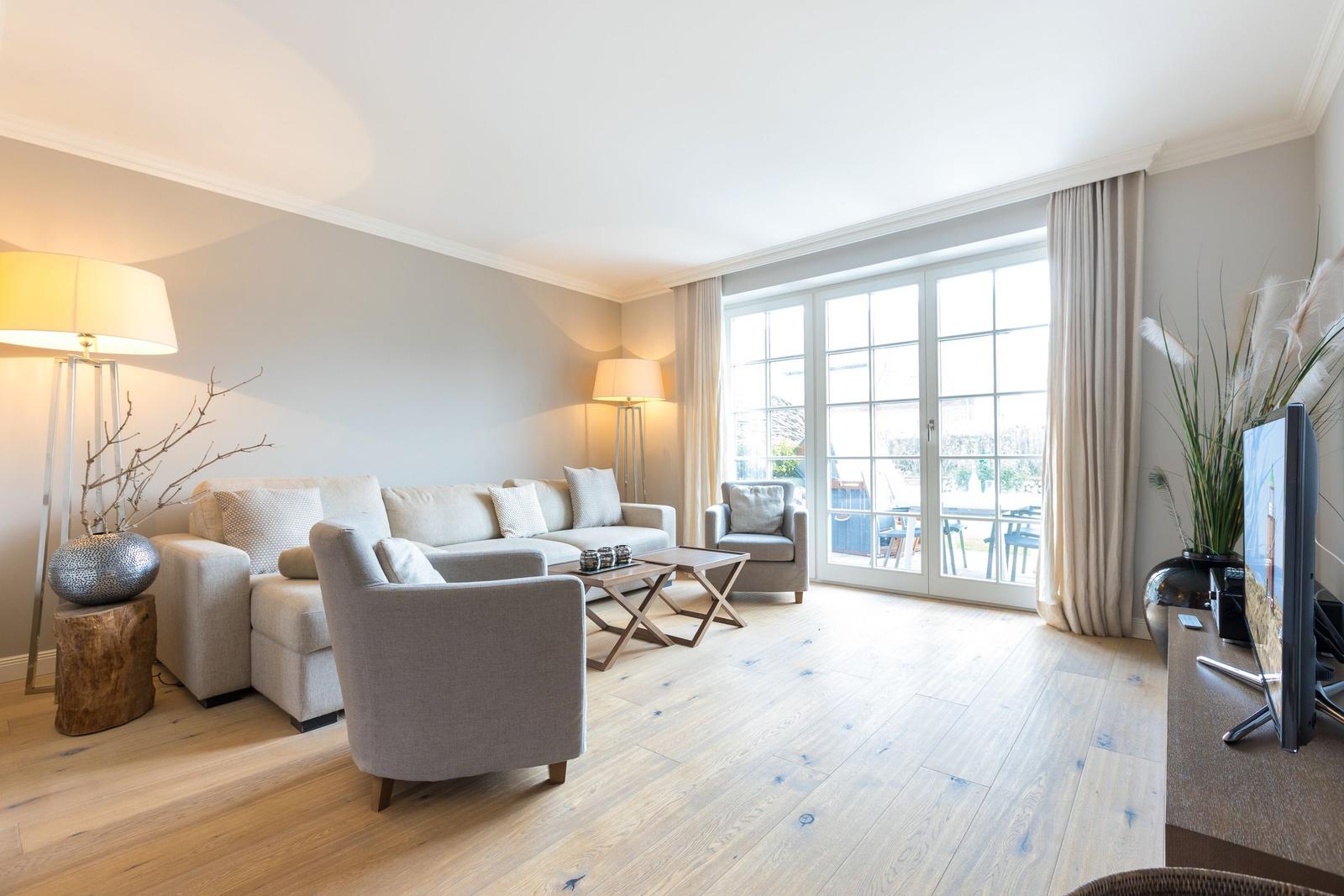 Living room with sofa, armchairs and wooden floor. Glass door leads to terrace.
