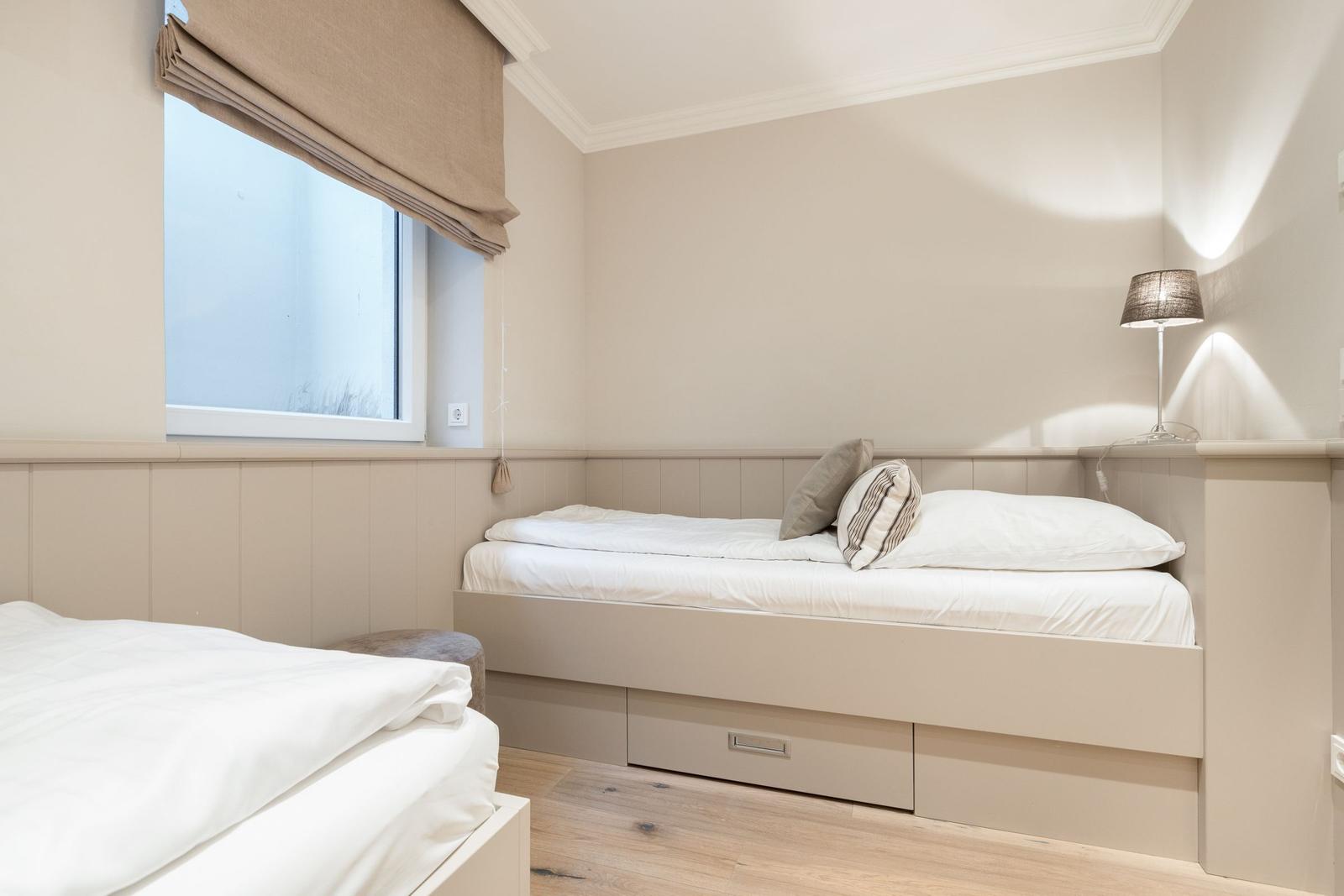 Bedroom with two beds, window, and bedside lamp.