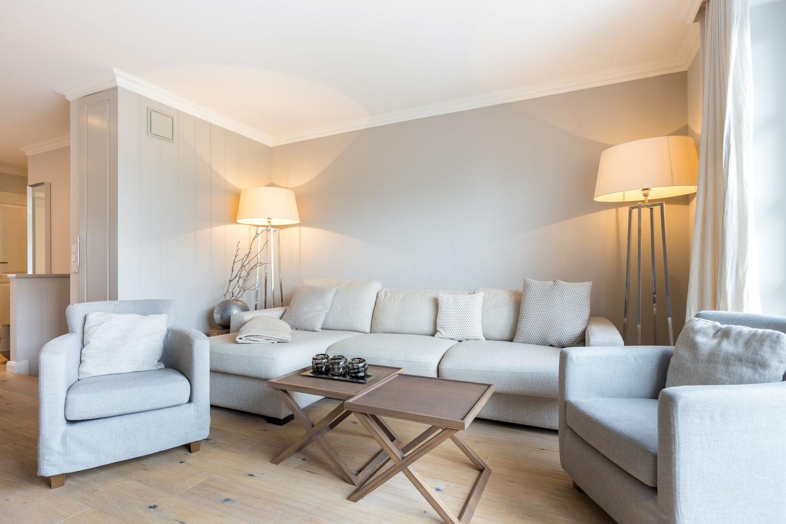 Living room with sofa, two armchairs, and wooden table. Lit by floor lamps.