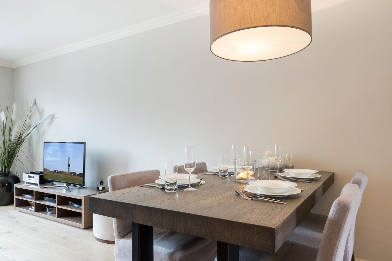 Dining table with chairs, table setting, and TV in background.