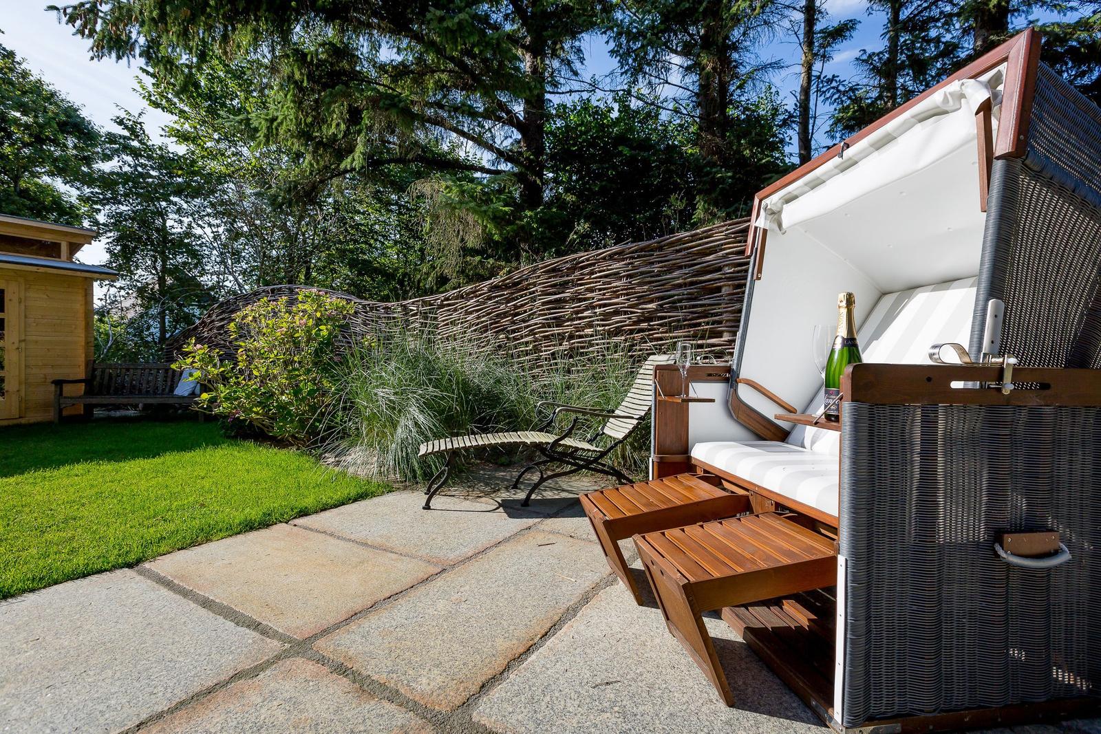 Outdoor area with lounger, table, and bottle of champagne. Background: grass, trees, and wooden wall.