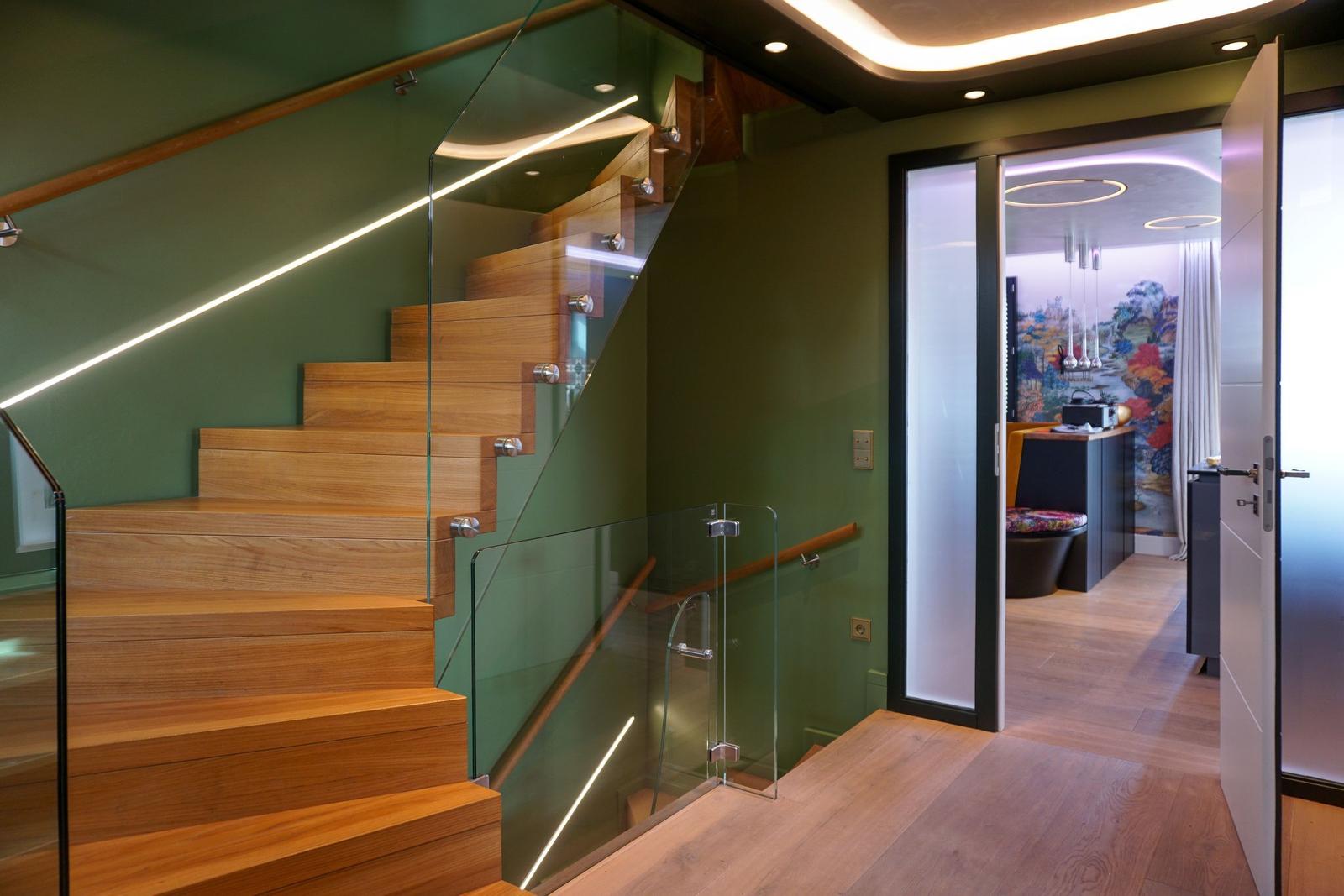 Wooden staircase with glass railing and green wall. Doorway to adjacent room.