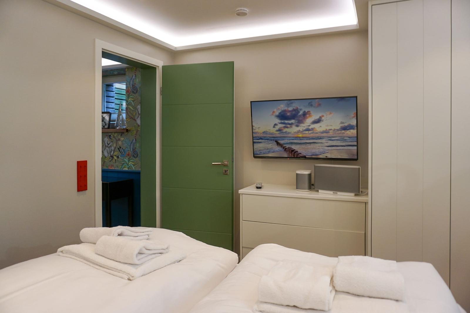 Two beds with towels, TV, and green door in the bedroom.
