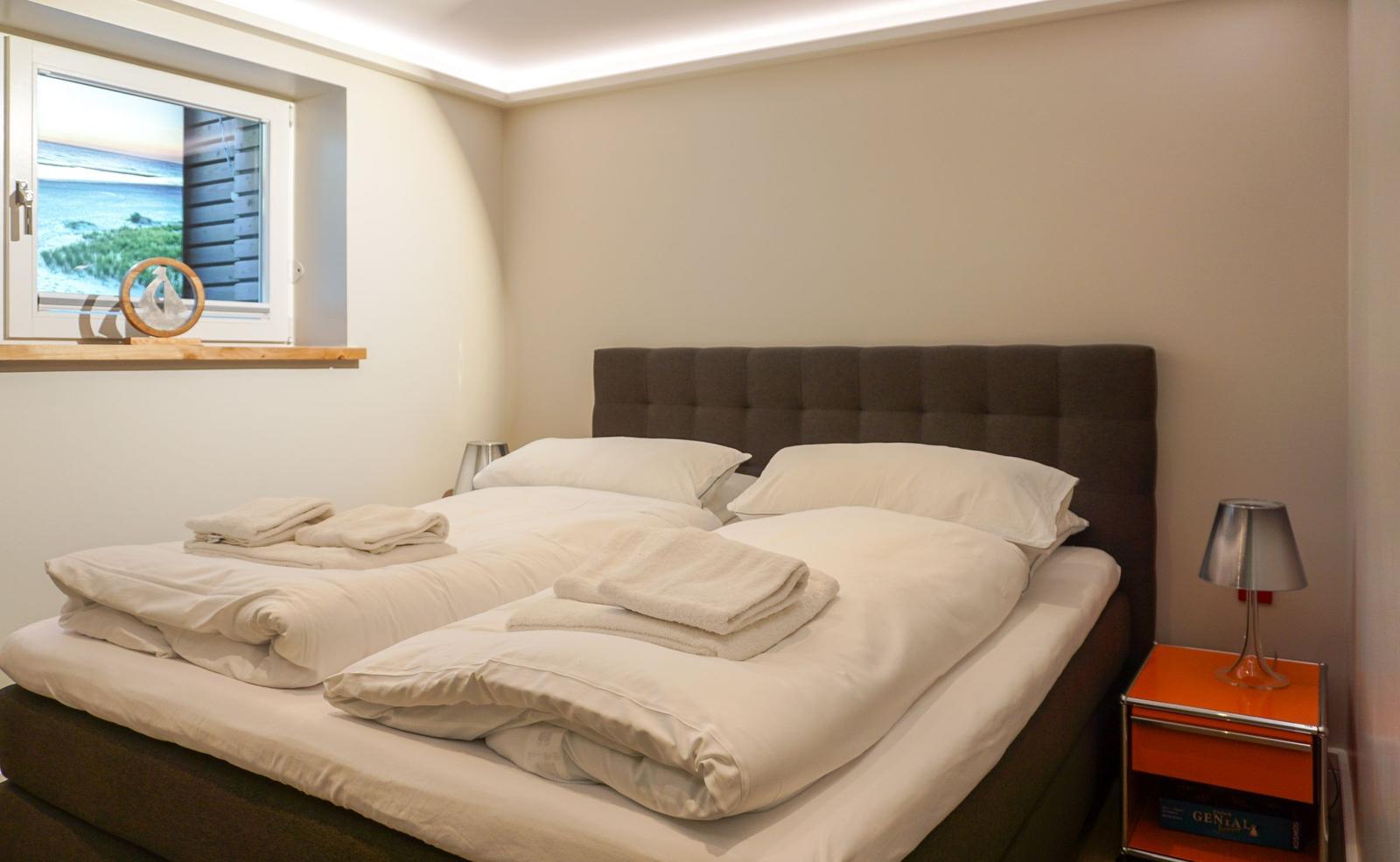 Bedroom with double bed, window with sea view, and nightstand with lamp.