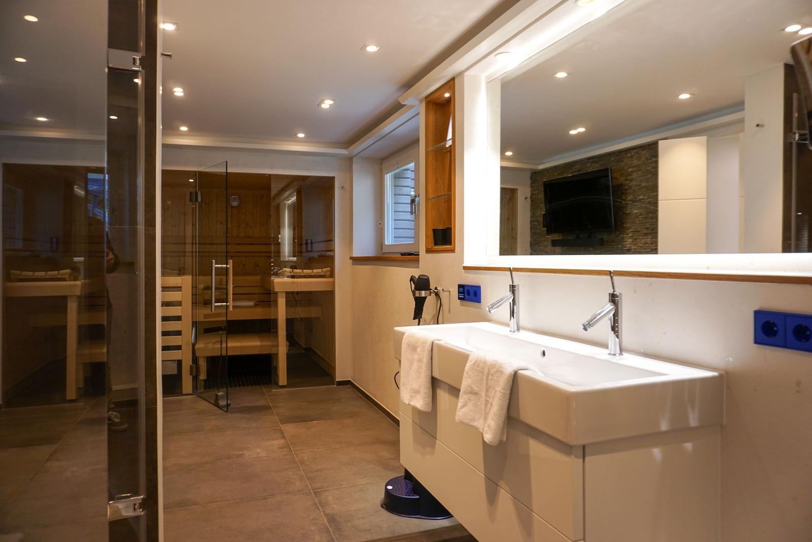 Bathroom with shower, sink, and sauna in the background.