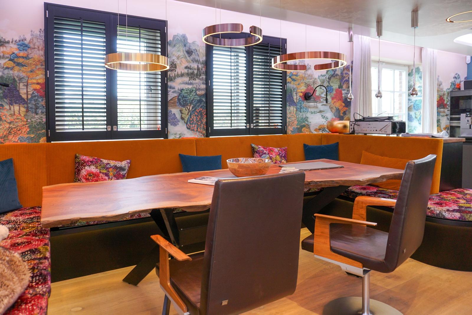 Dining area with wooden table, orange booth, and modern pendant lights.