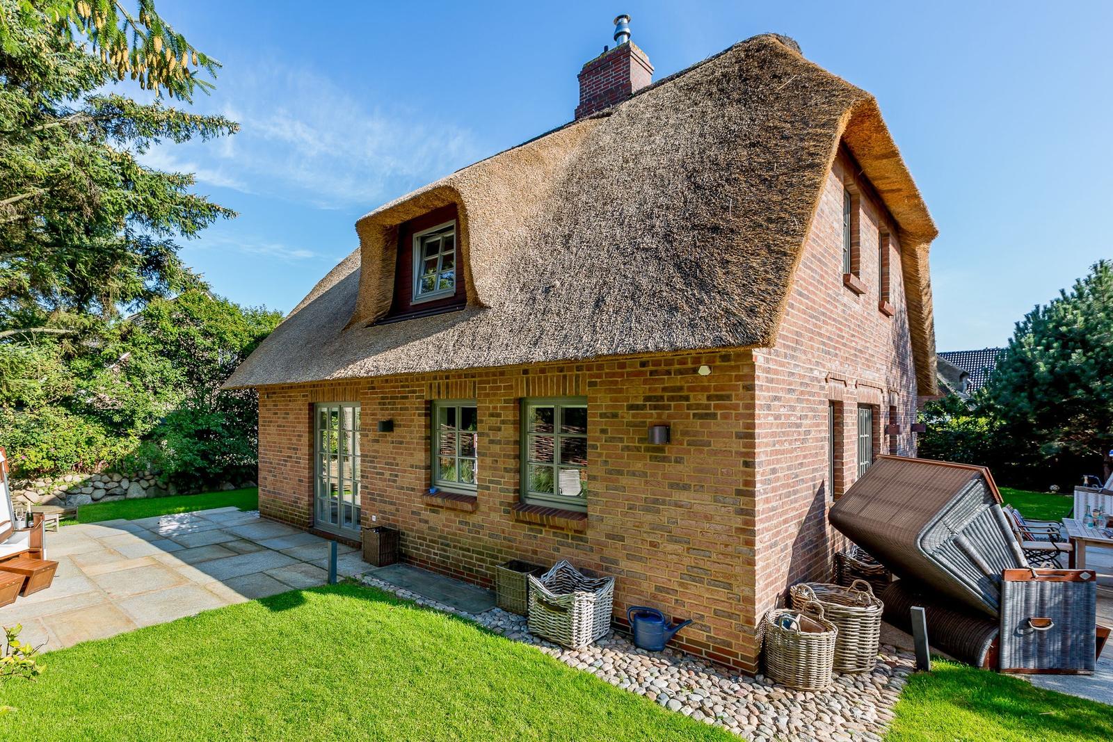 A thatched roof house with brick facade and garden area.