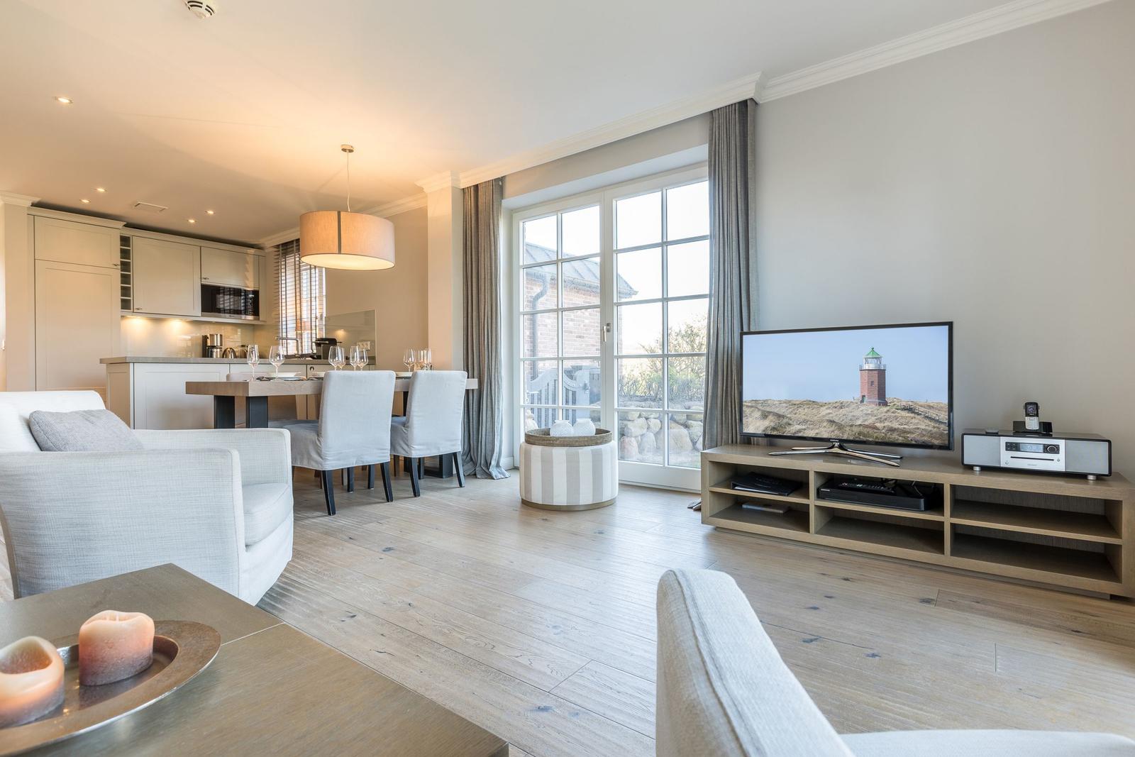 Living room with dining area and TV. Wooden floor and large windows.