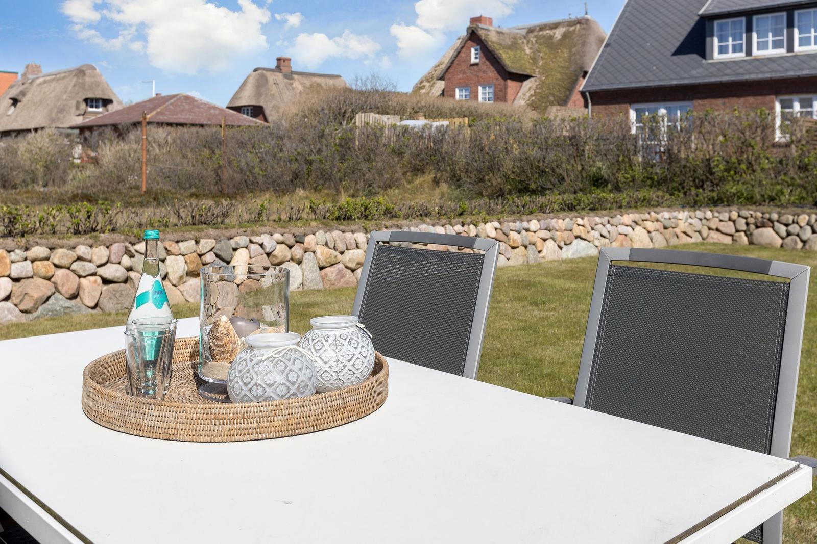 Outdoor area with table, chairs, and decorative items. Houses and stone wall are visible in the background.
