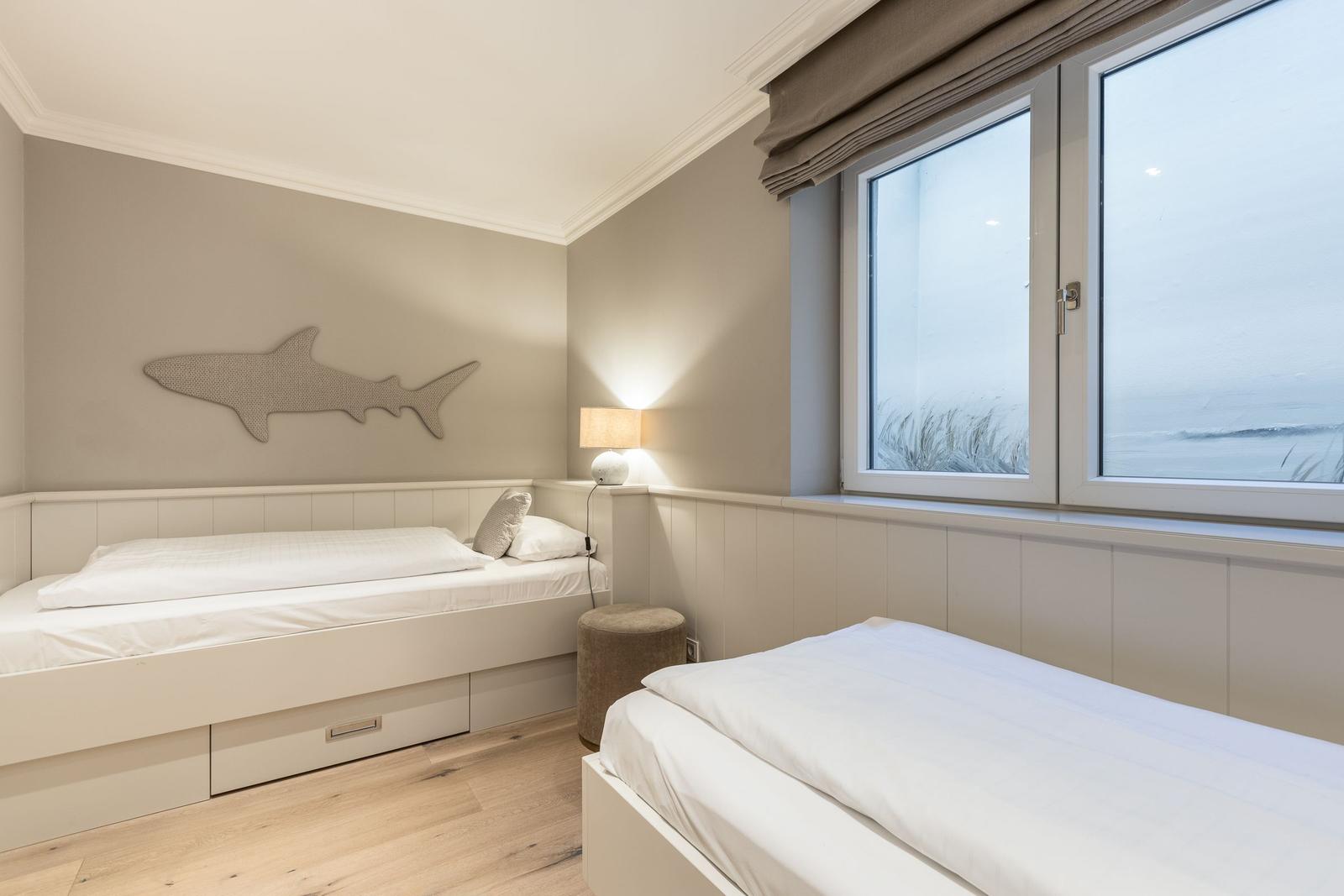 Room with two beds, shark wall decor, and sea view through window.