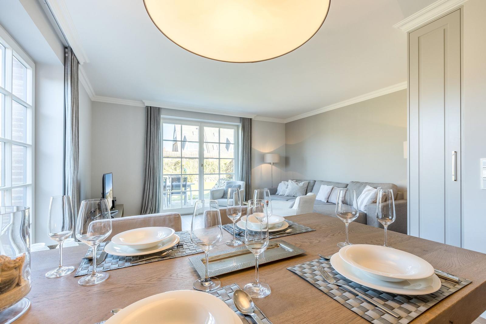 Dining room with table, glasses, and plates. Living area with sofa and window in background.