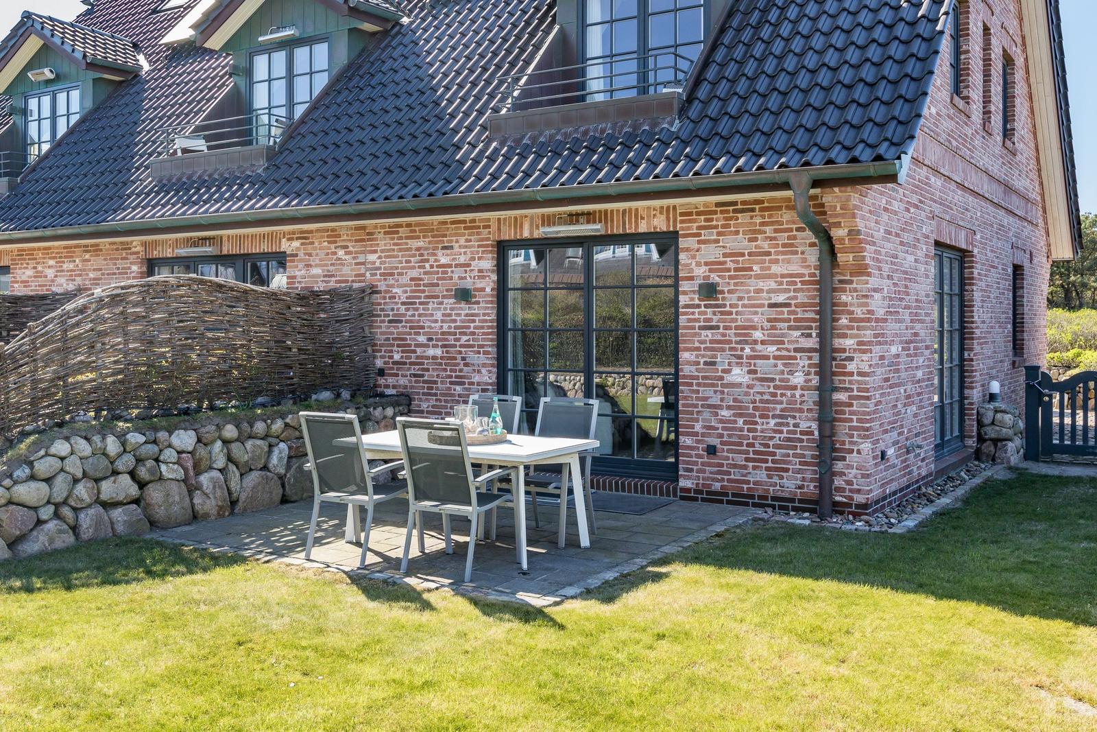 Terrace with table and chairs in front of a brick house with dark roof.