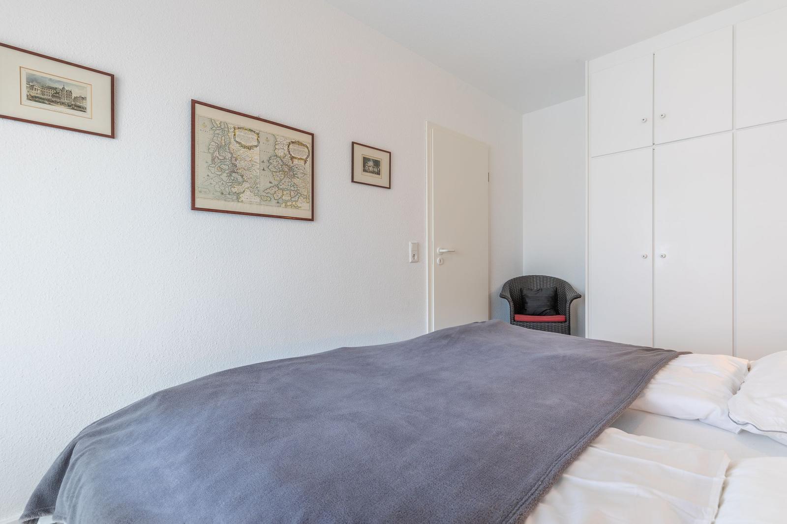 Schlafzimmer mit Bett, Kleiderschrank und Wandbildern.