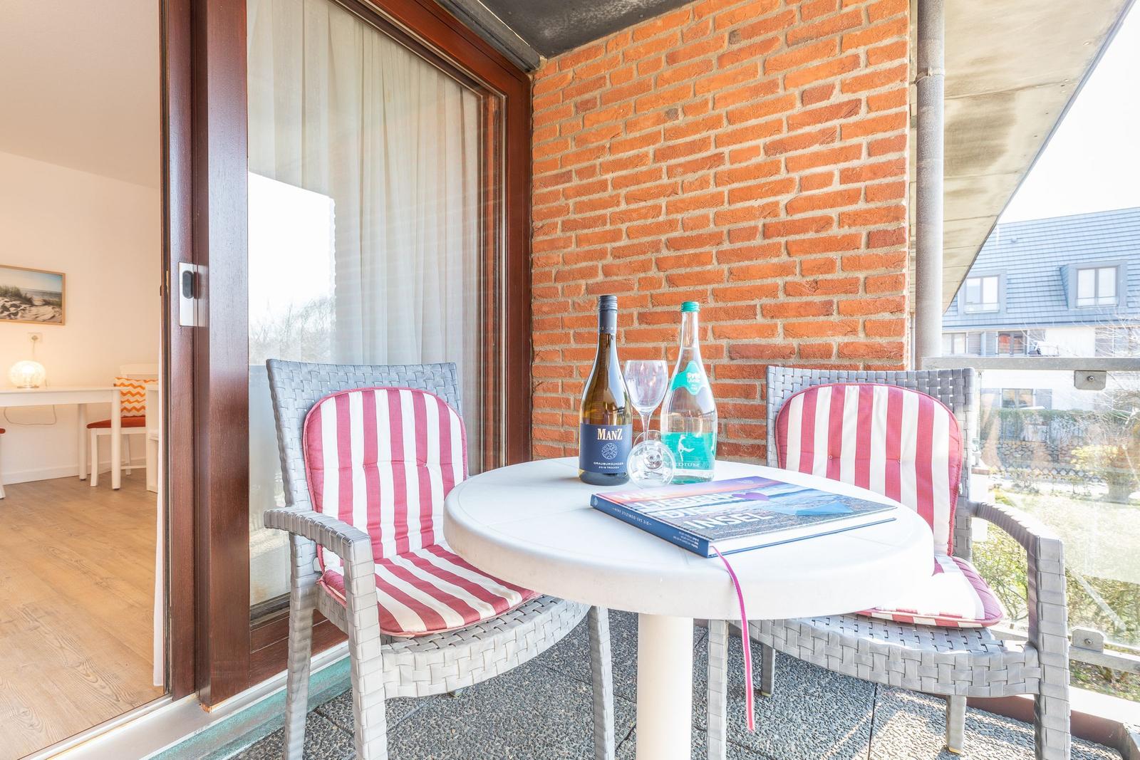 Terrasse mit Tisch, zwei Stühlen und Getränken. Im Hintergrund ist ein Wohnraum sichtbar.