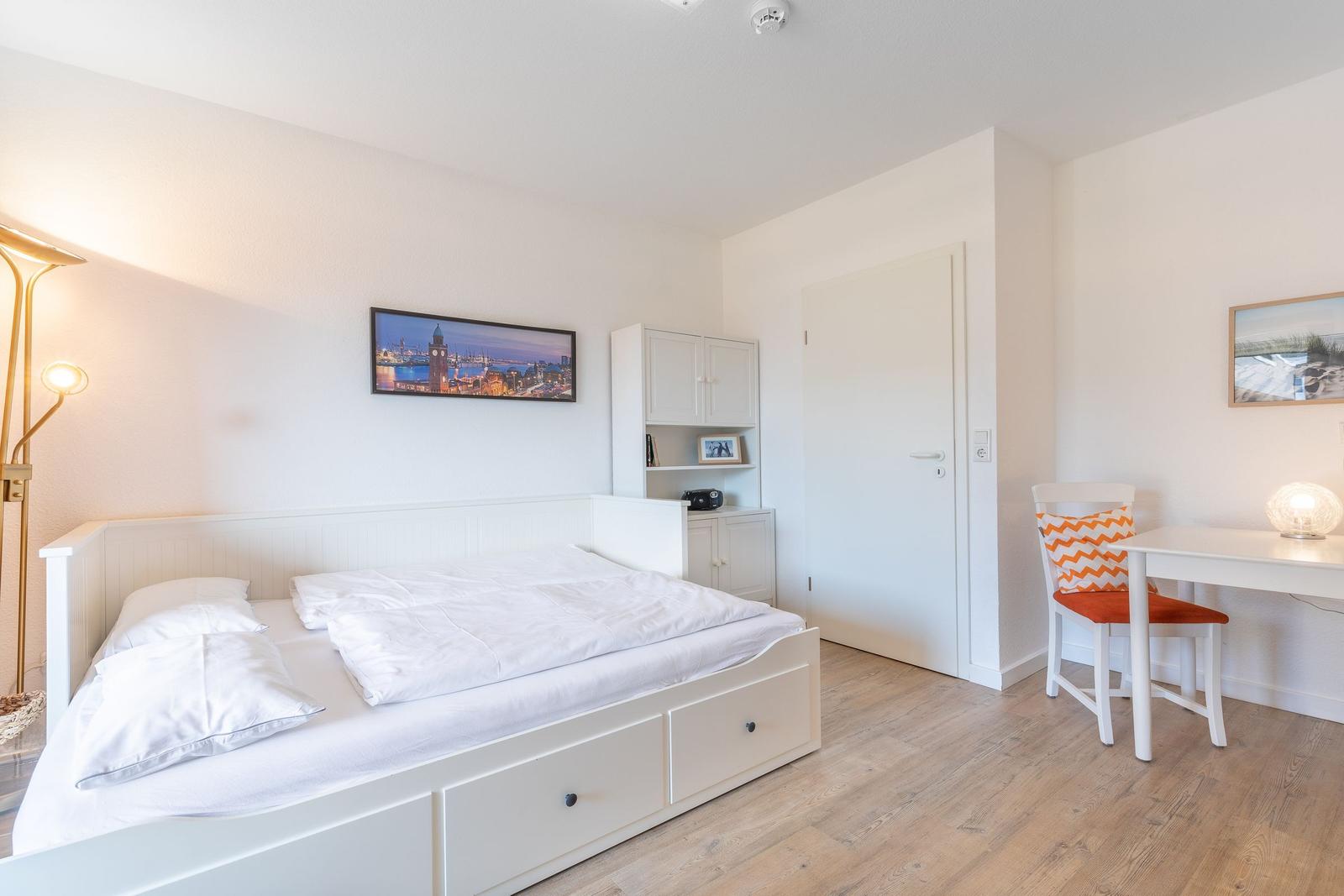 Schlafzimmer mit Bett, Schreibtisch und Wandbild.