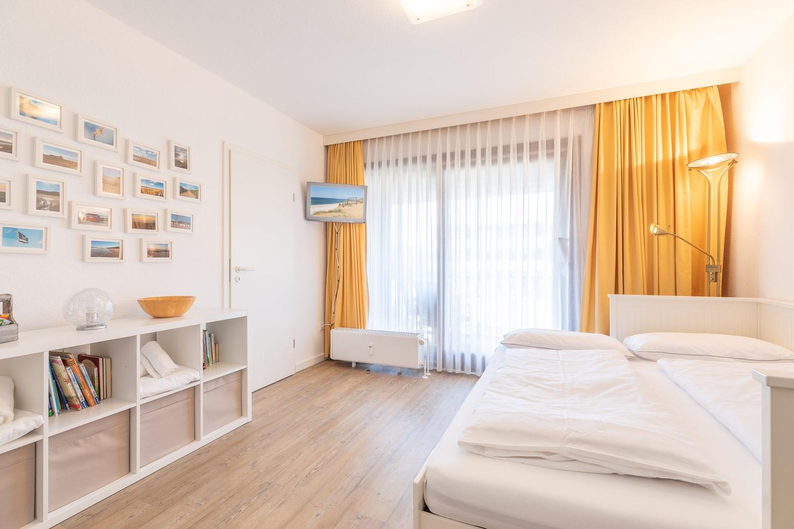 Schlafzimmer mit Doppelbett, gelben Vorhängen und Wandbildern.