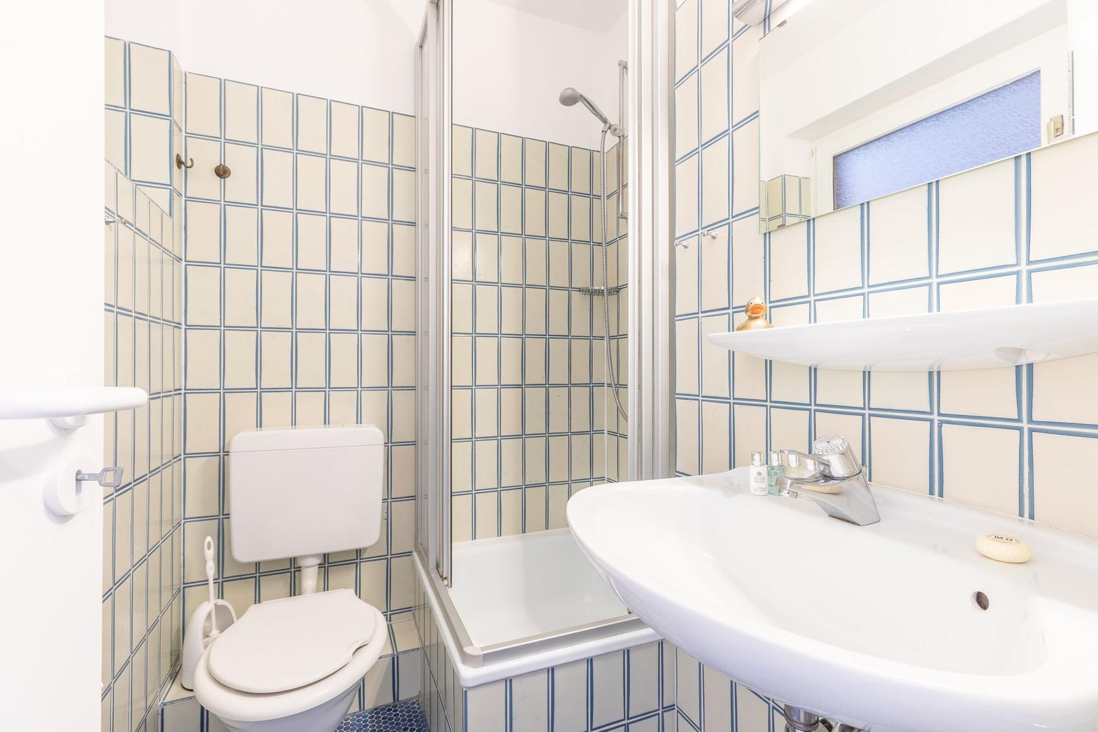 Badezimmer mit Dusche, Toilette und Waschbecken. Fliesen mit blauen Linien.