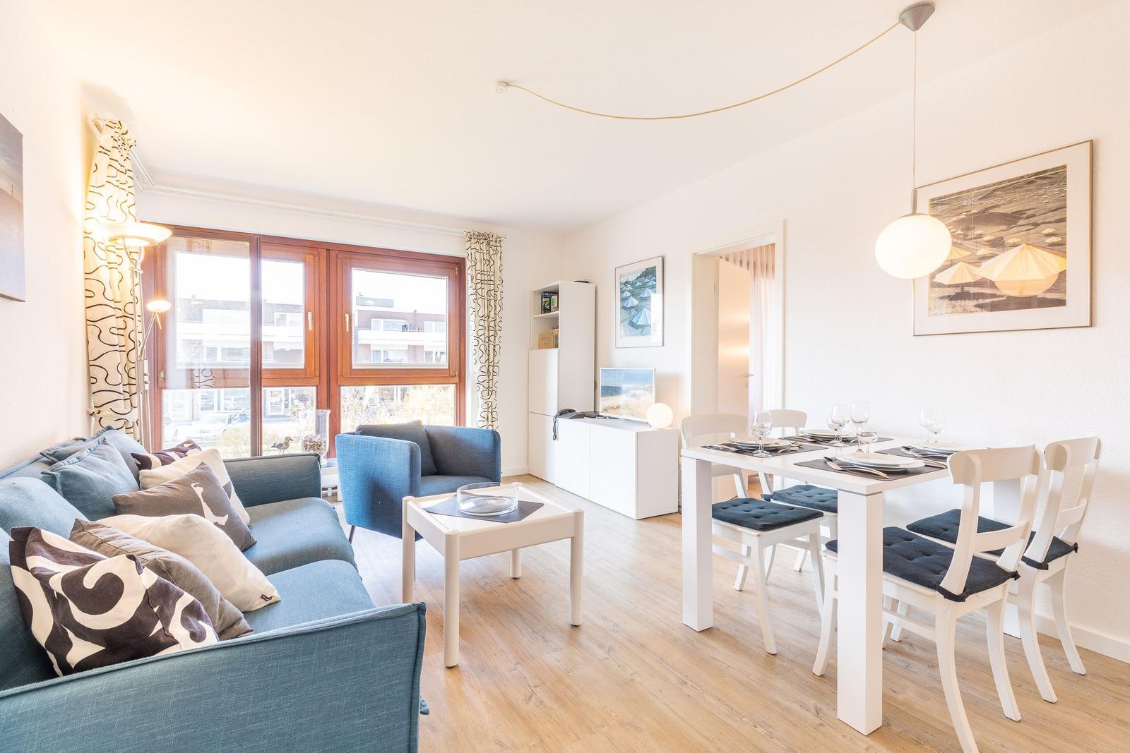 Wohn- und Essbereich mit Sofa, Tisch und Stühlen. Holzboden und Fenster.