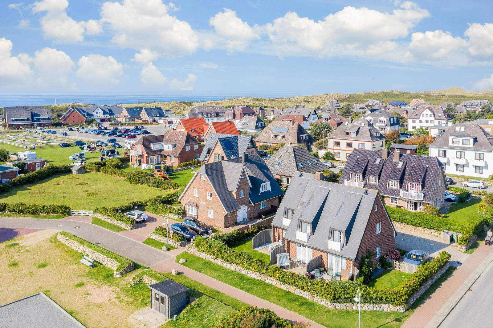 Houses with gardens and parking lots near the coast under blue sky.