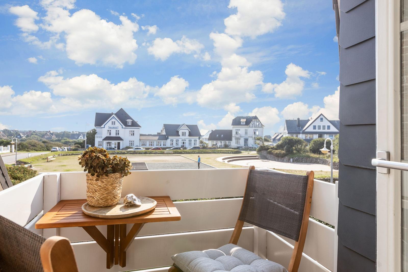 Balcony with chair and table, view of white houses and blue sky.