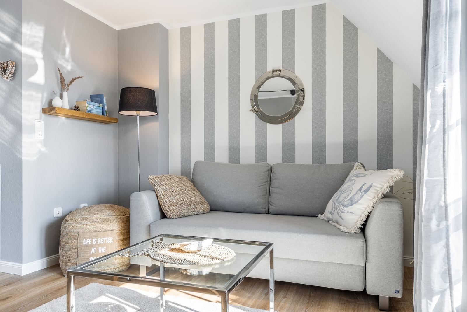 Living room with gray sofa, striped wall, and round mirror.