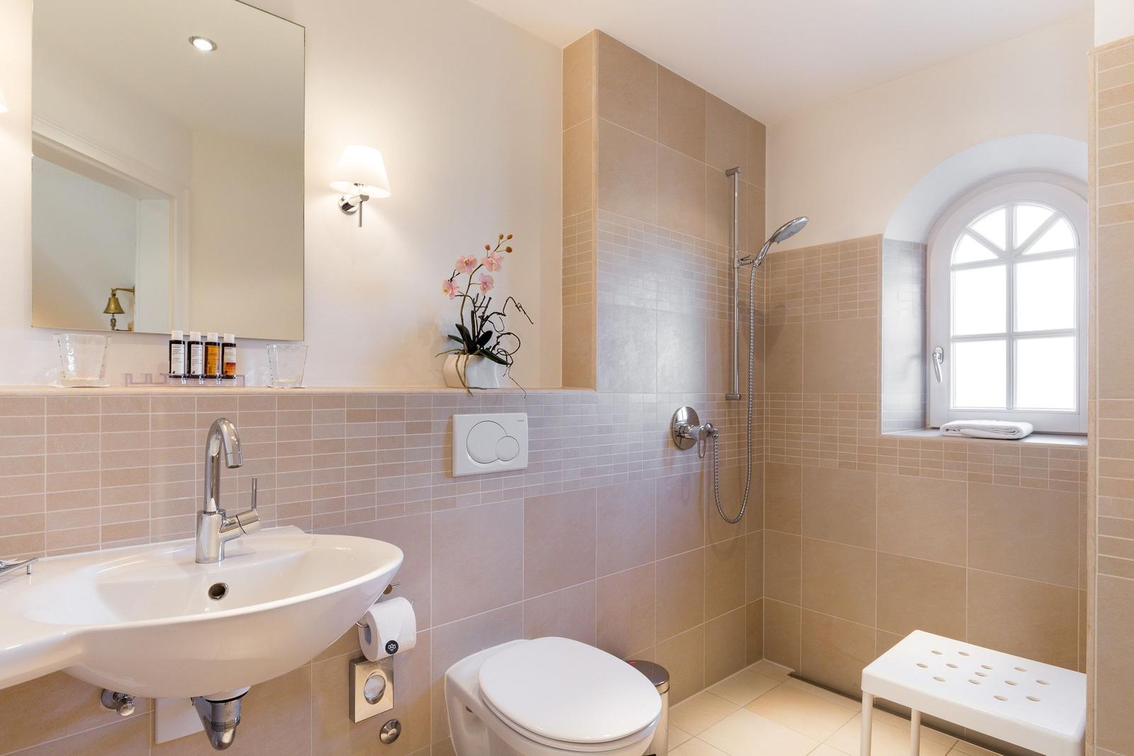 Bathroom with shower, sink, and toilet. Window with arched frame.