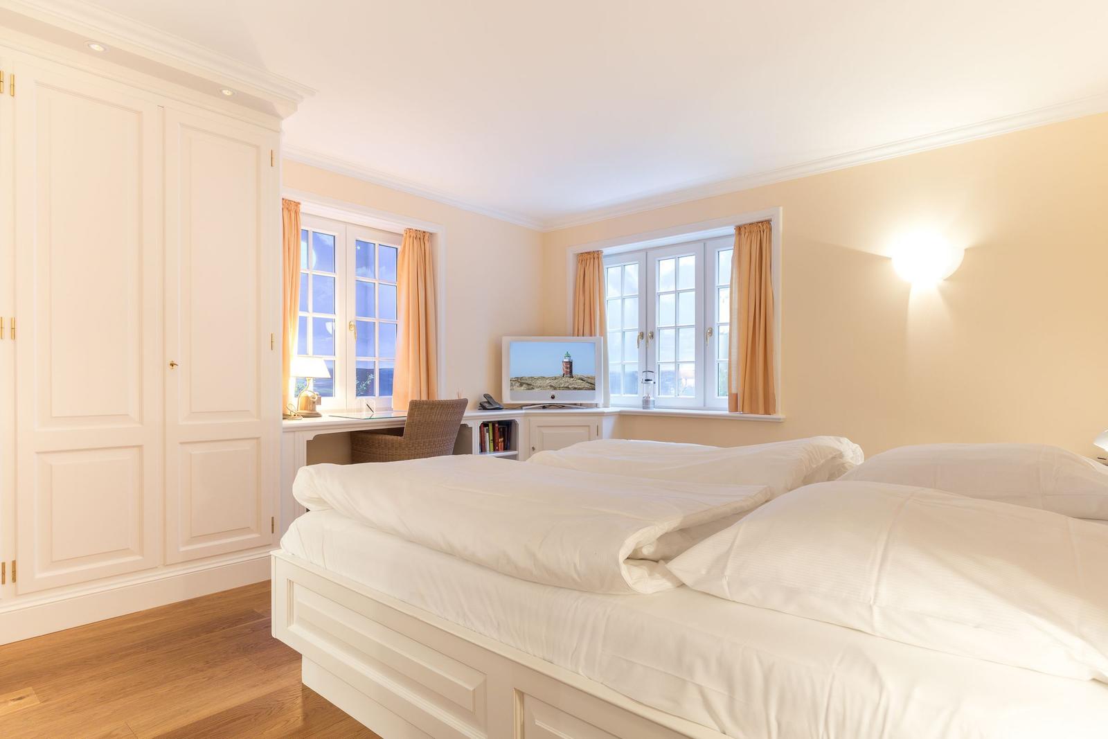 Bedroom with double bed, desk, and two windows with curtains.
