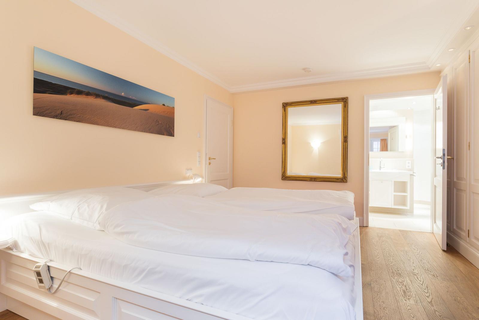 Bedroom with white bed, wall art, and view into the bathroom.