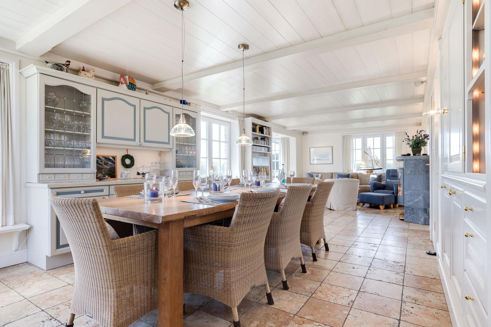 Dining room with wooden table, chairs, and kitchen area. Living area with sofa and fireplace in the background.