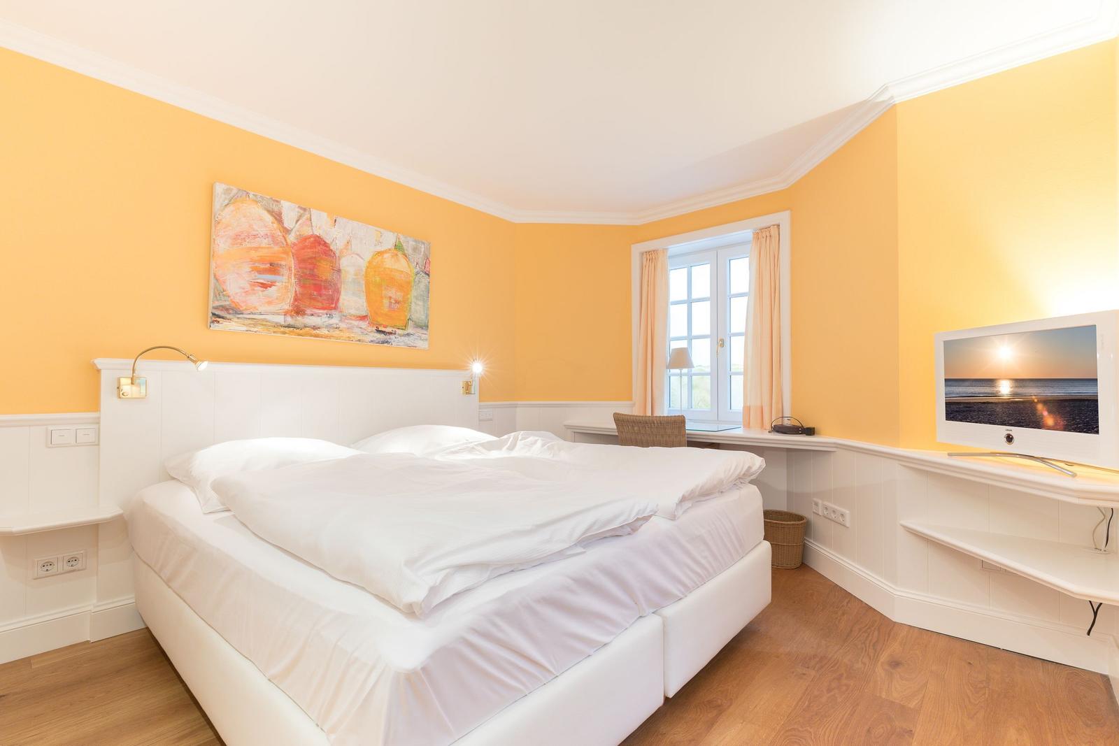 Bedroom with double bed, window, TV and wall art.