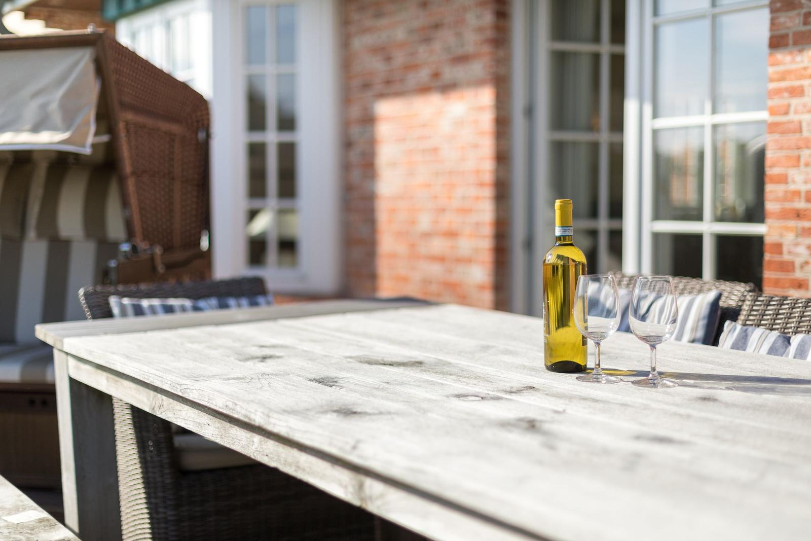 Outdoor area with table, wine bottle, and two glasses in front of brick wall and windows.
