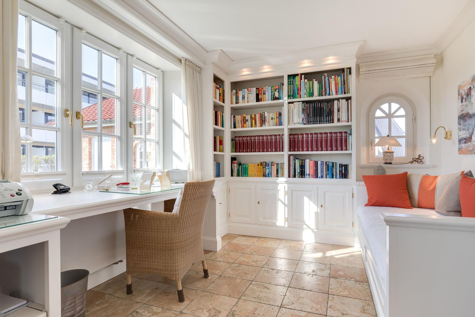 Home office with bookcase, windows, and seating bench.