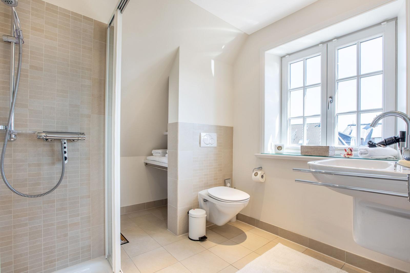 Badezimmer mit Dusche, Toilette und Waschbecken. Fenster mit Blick auf Dächer.