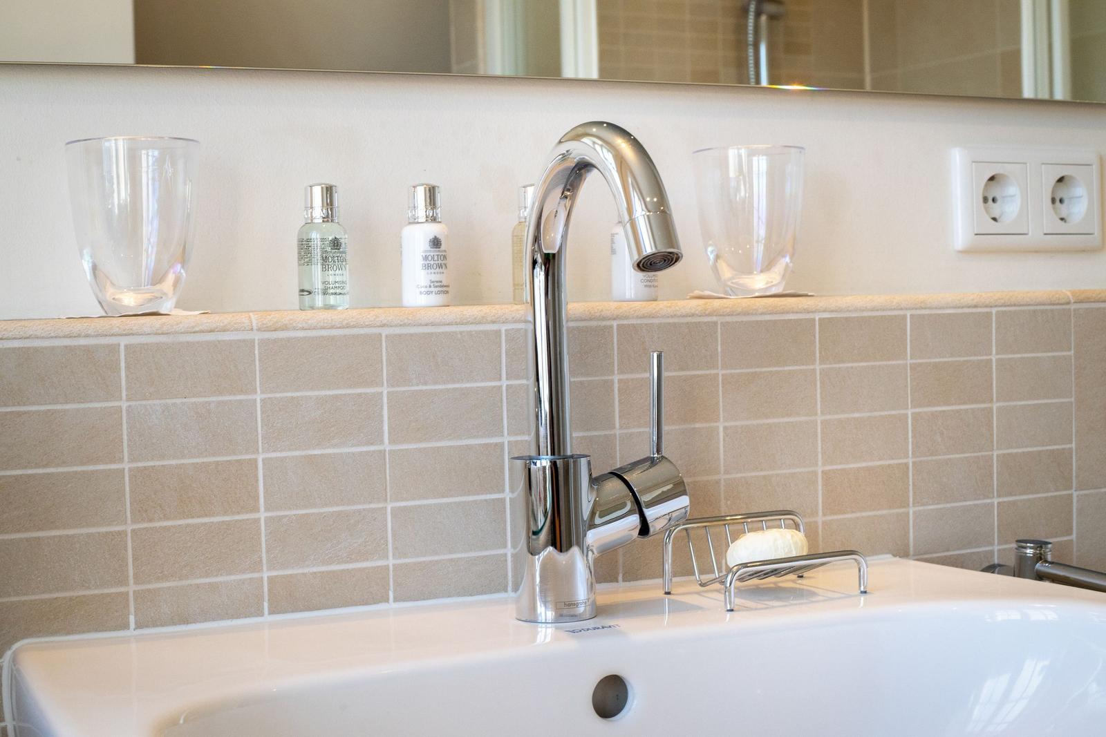 Waschbecken mit modernem Wasserhahn und Flaschen auf der Ablage.