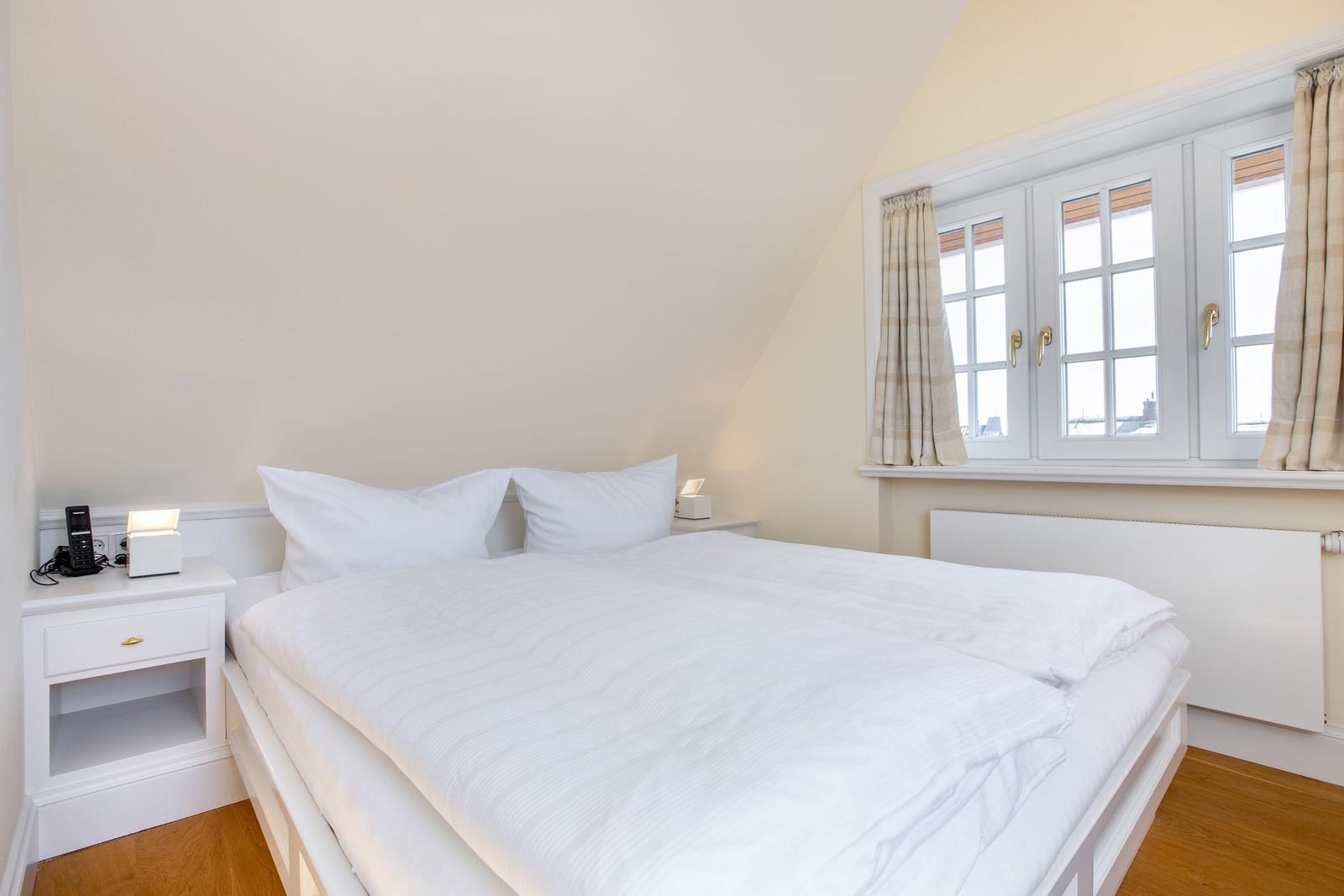 Schlafzimmer mit Doppelbett, Fenster und Nachttisch.