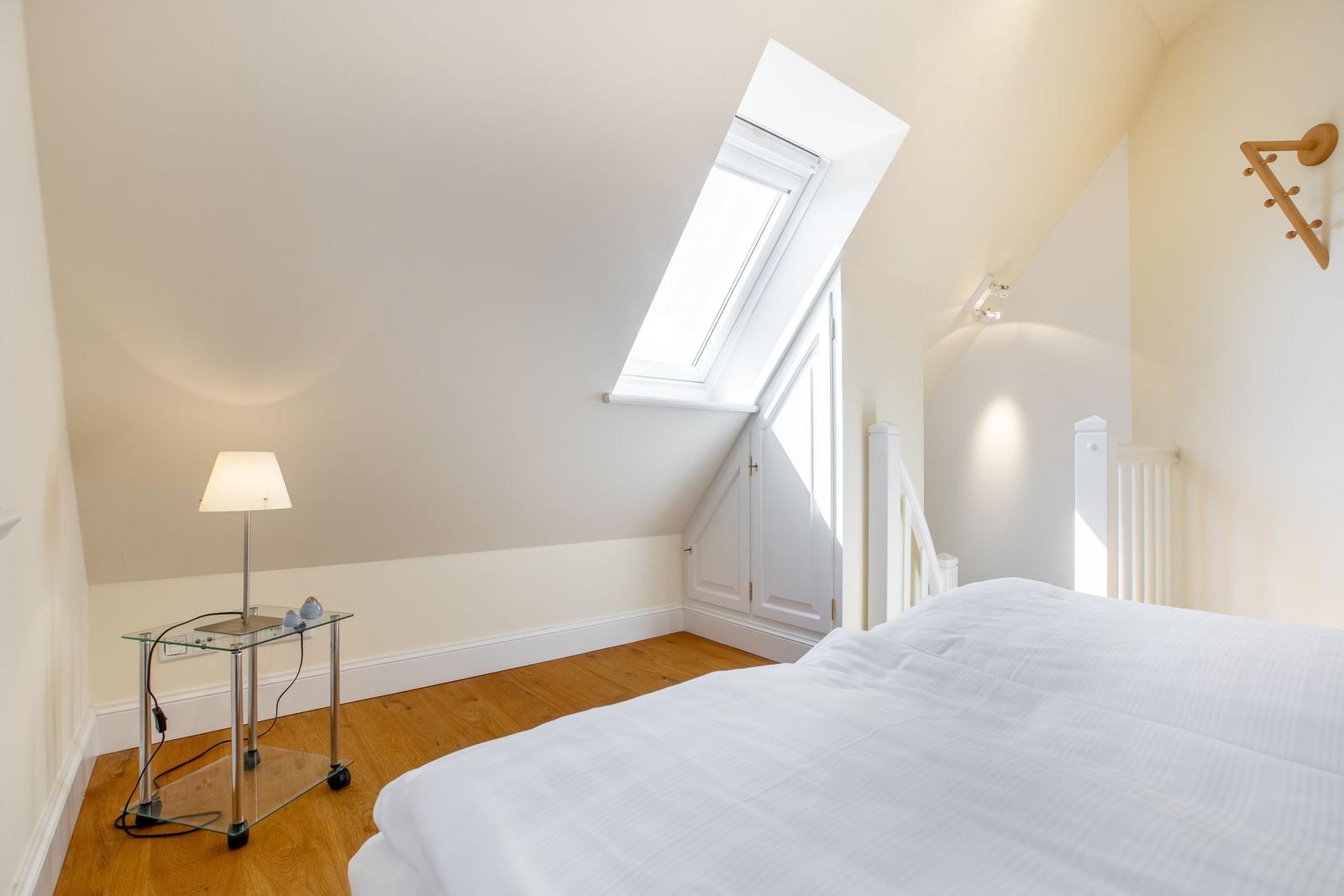 Schlafzimmer mit Dachschräge, Dachfenster, Bett und Nachttisch.