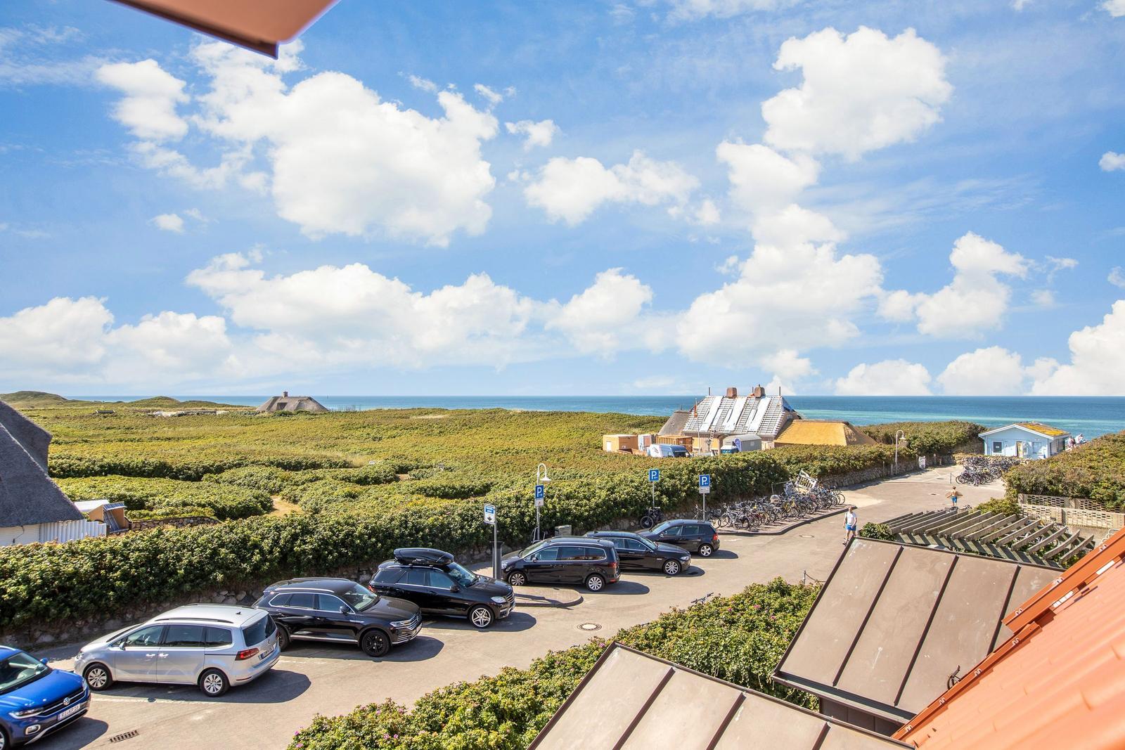 Parkplatz mit Autos und Blick auf das Meer und grüne Dünen.