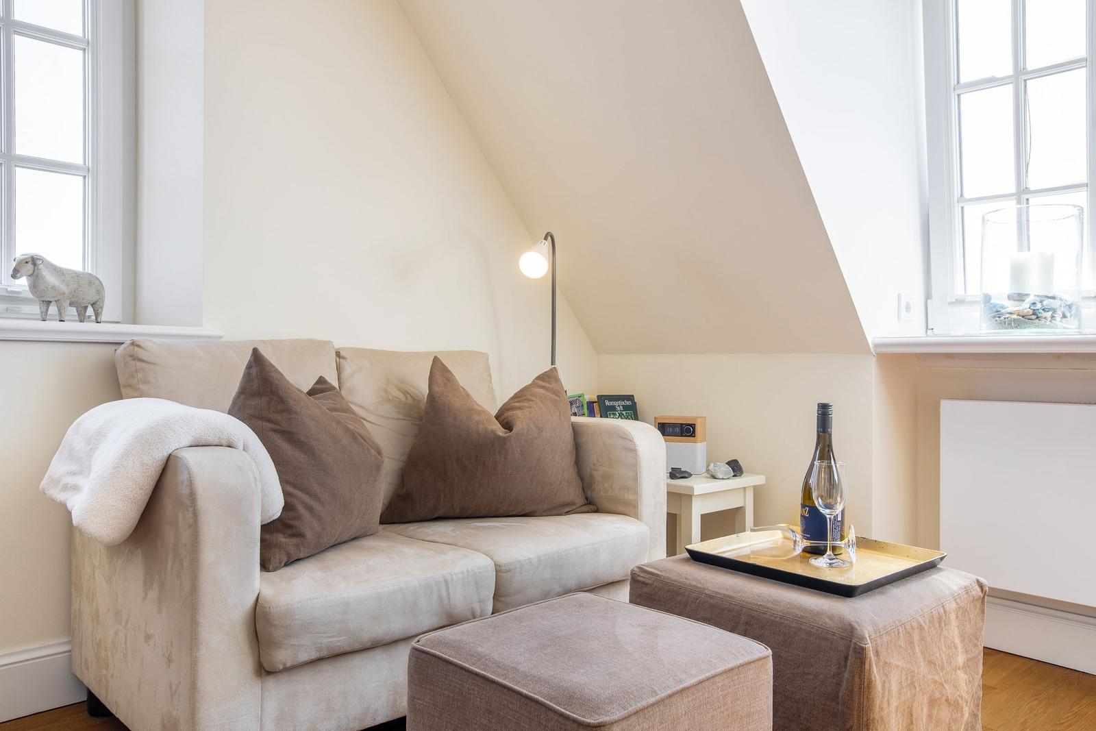 Ein Sofa mit Kissen und Decke unter einem Dachschrägenfenster mit Tisch und Wein.
