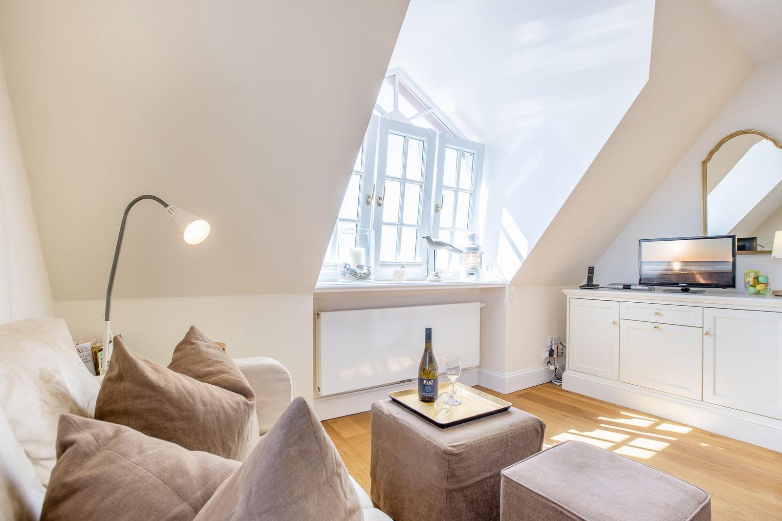 Wohnzimmer mit Dachschrägen, Fenster, Sofa, Beistelltisch und Fernseher.