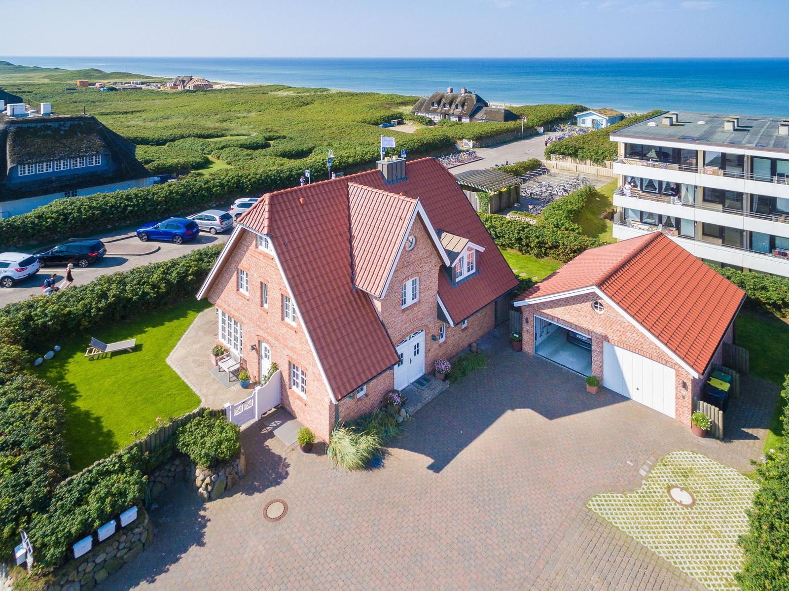 Rotes Ziegeldach, gepflasterter Hof, Garten und Blick aufs Meer.