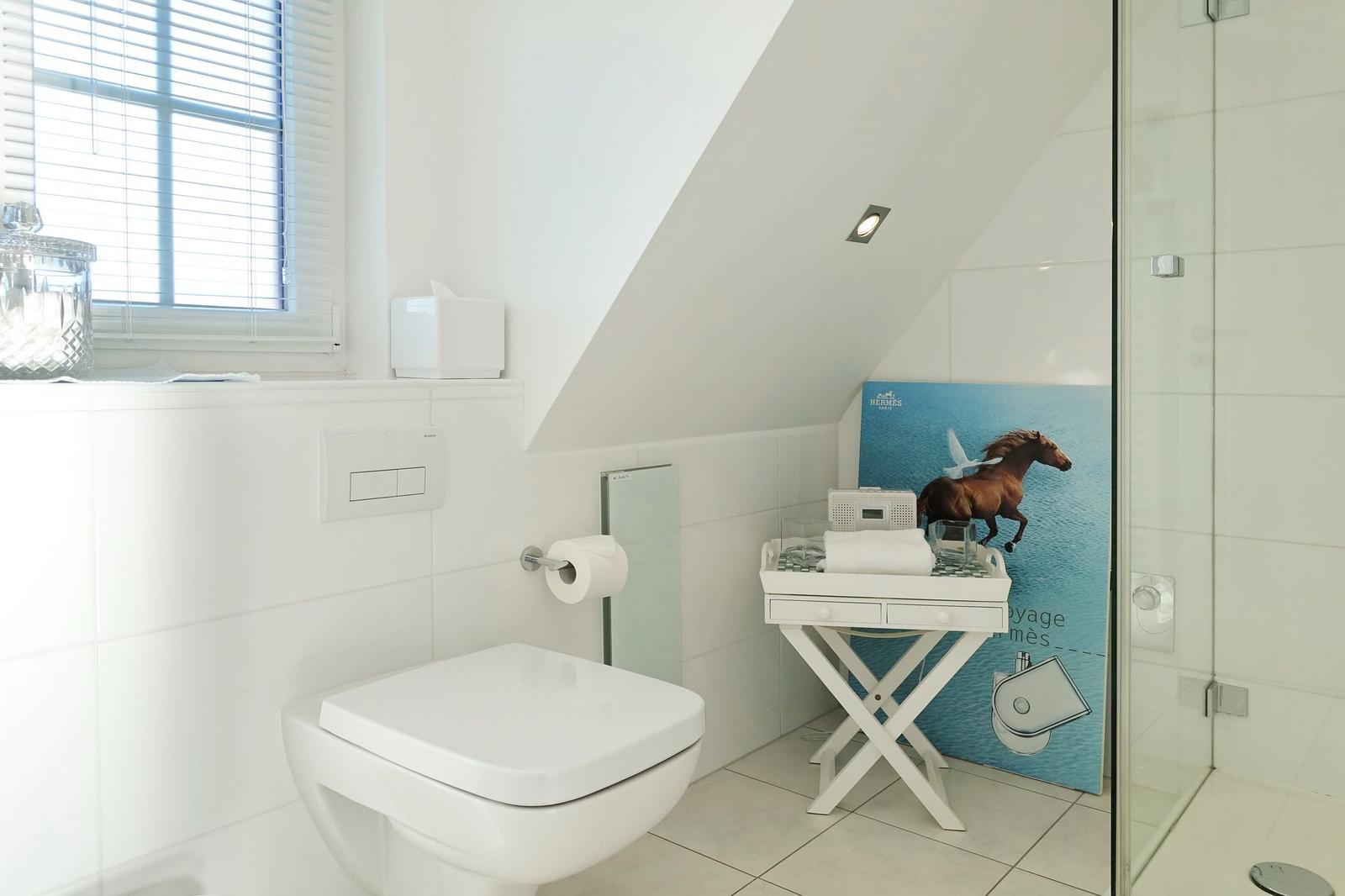 Bathroom with toilet, shower, and window with blinds.