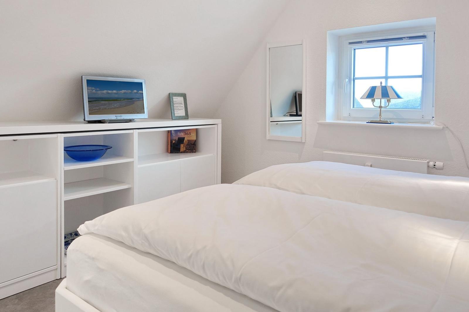 Bedroom with white bed, TV, and window with lamp.