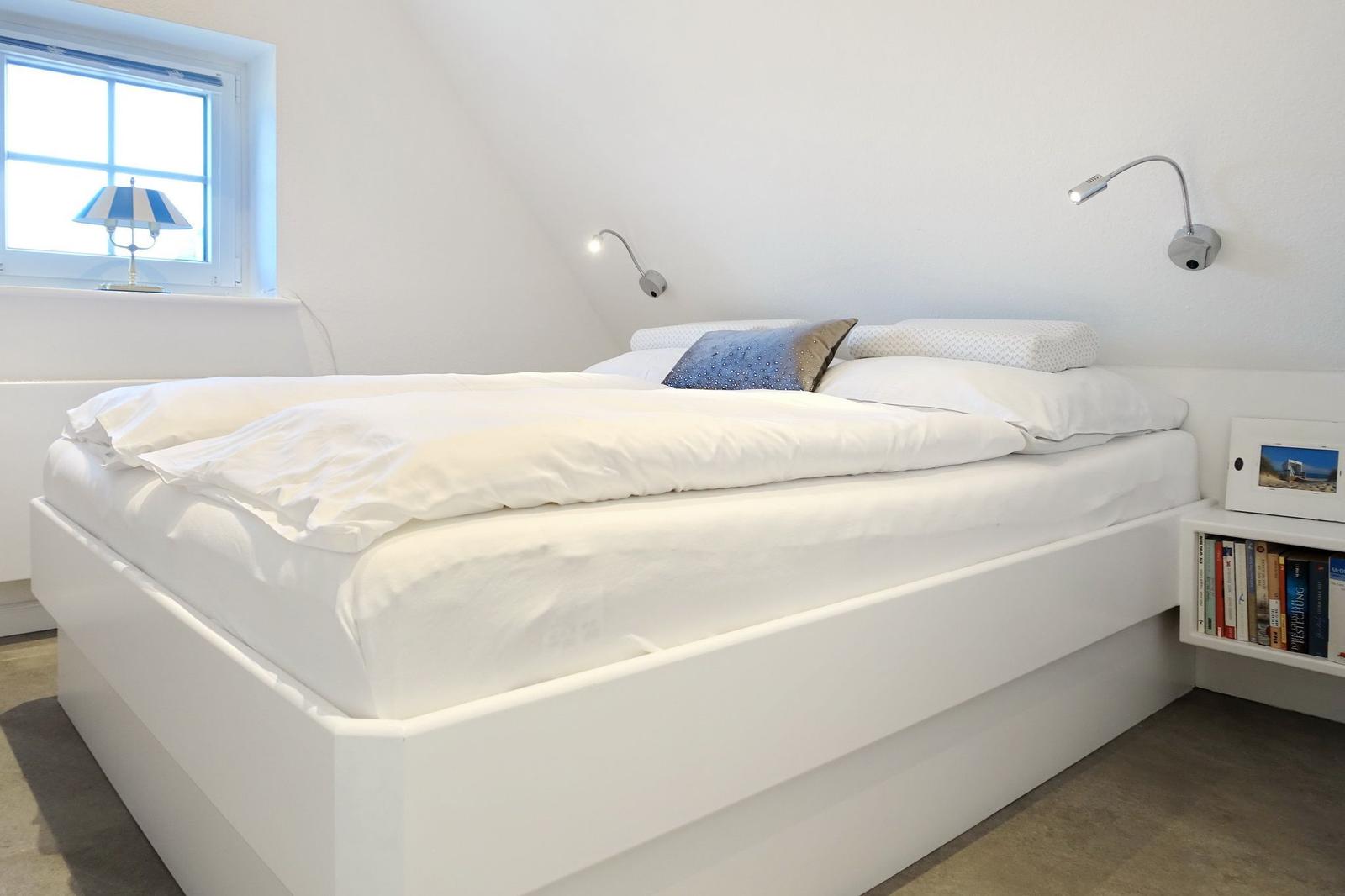 Bedroom with white bed, window, and table lamp.