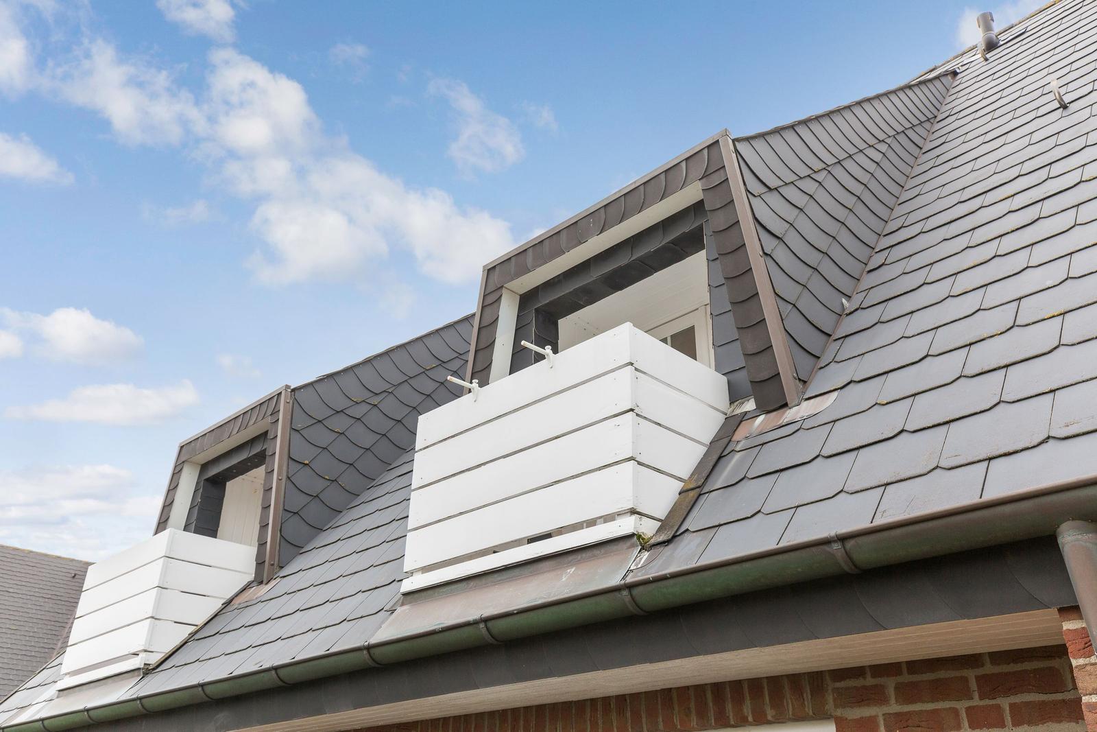 Attic with white balconies and gray slate roof under blue sky.