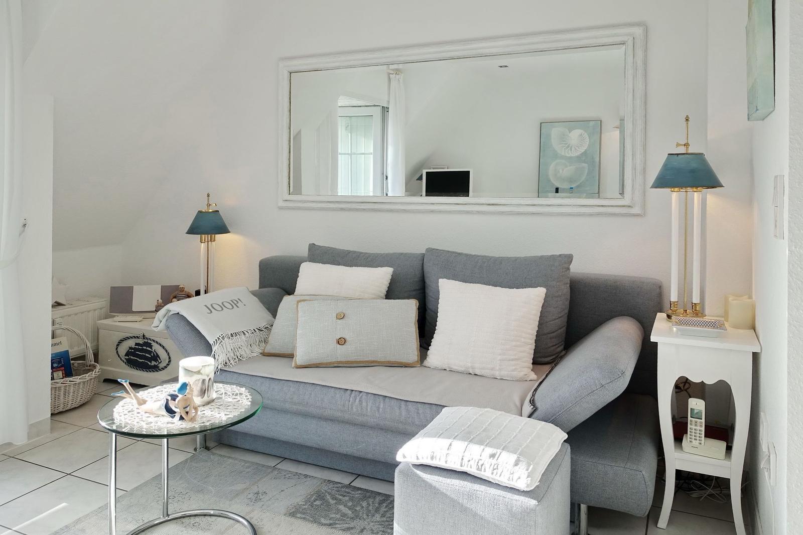 Gray sofa with cushions, mirror on wall, side tables and coffee table.