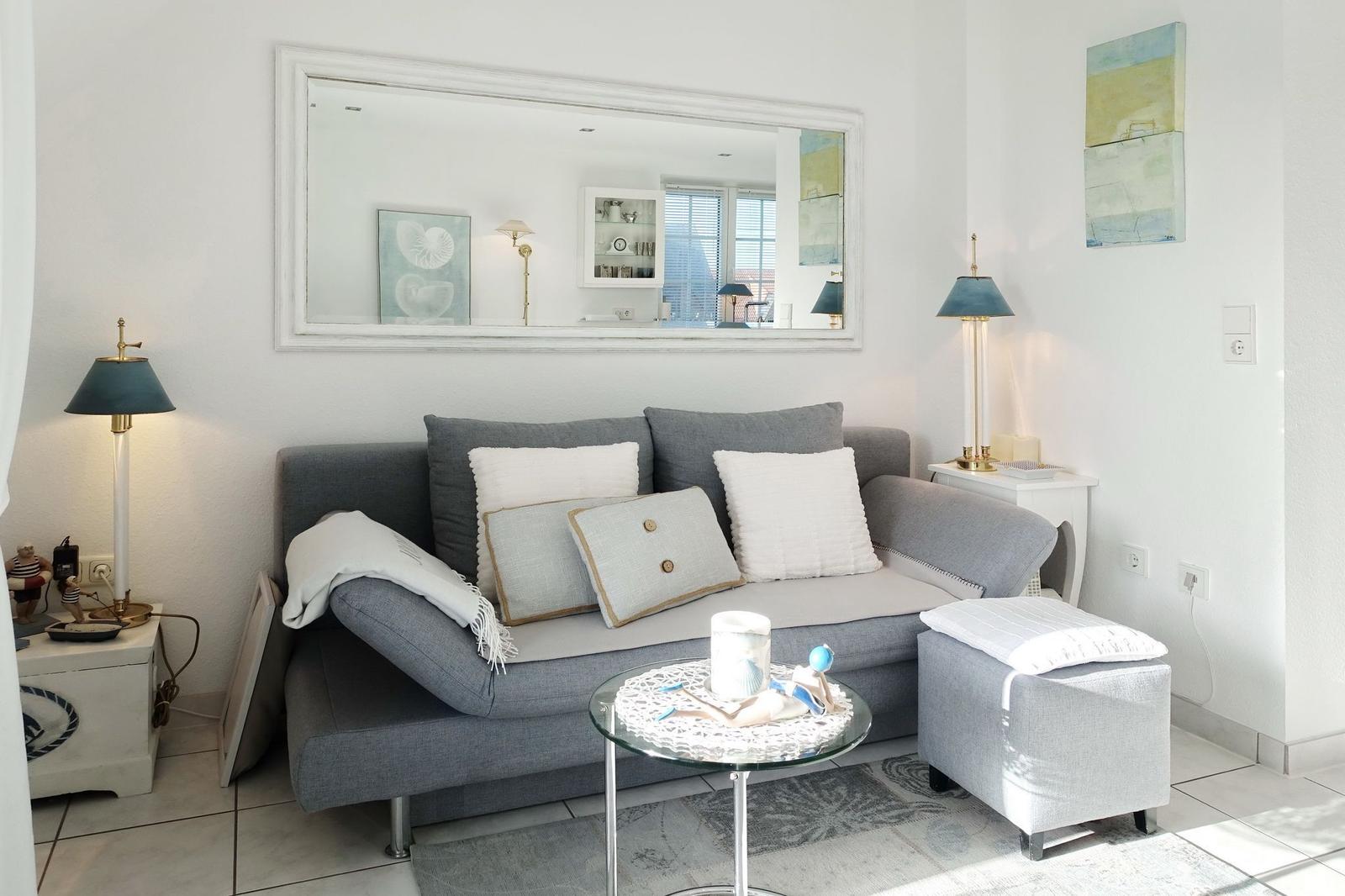 A living room with a gray sofa, cushions, and a mirror on the wall.
