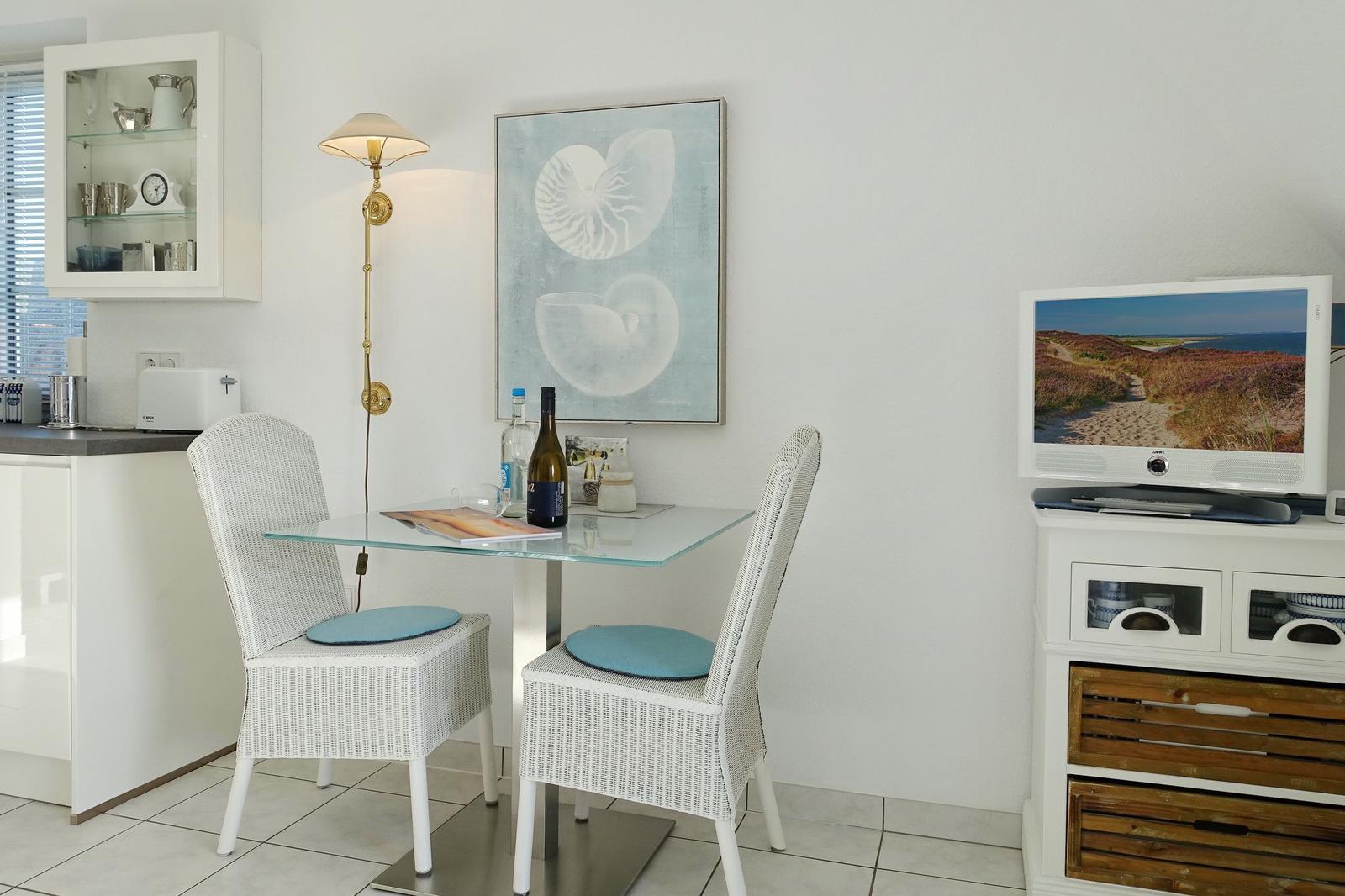 Dining area with table, two chairs, and TV. Wall art shows shells.