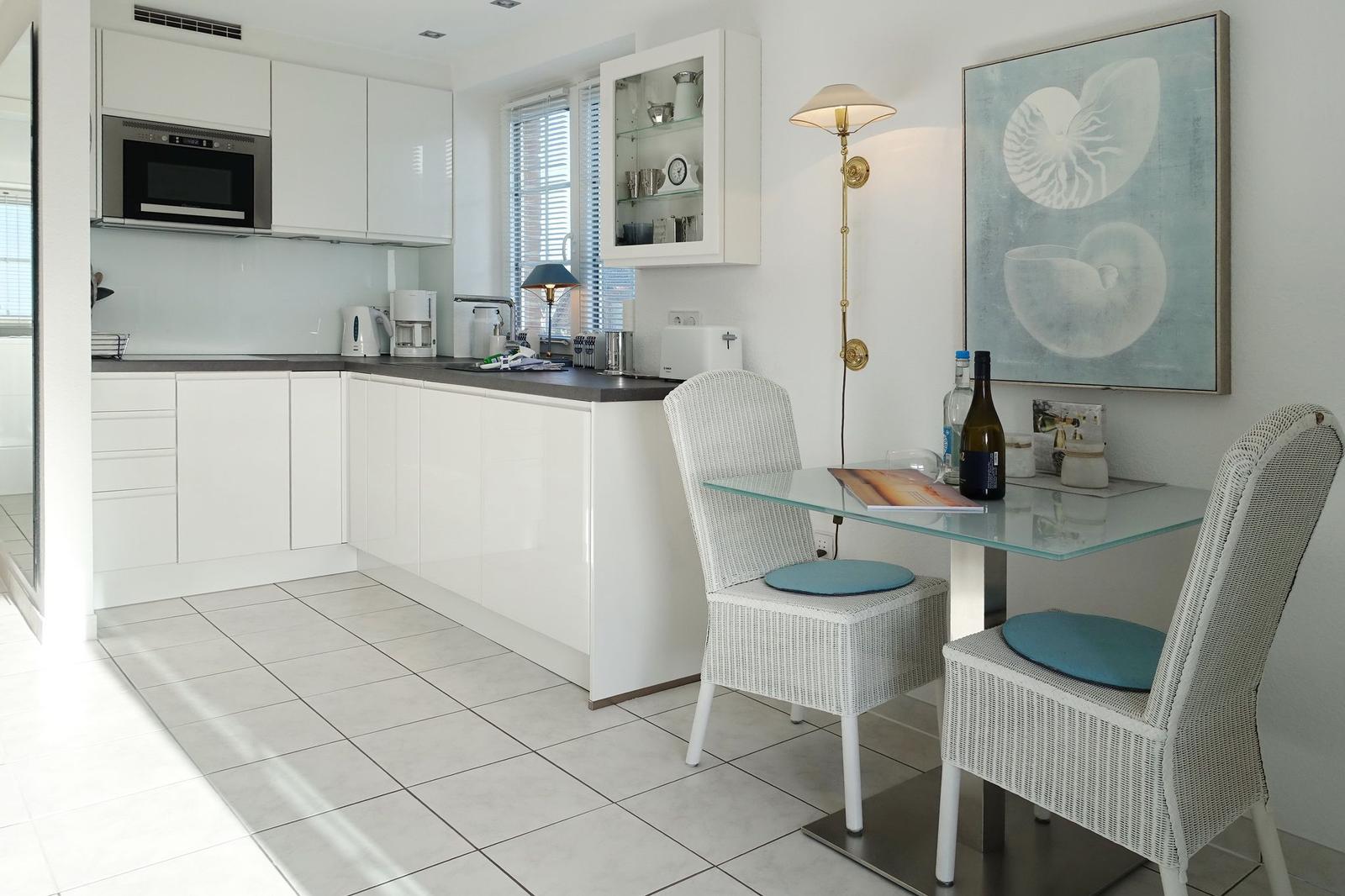Kitchen with dining area, white cabinets, glass top, and chairs with blue cushions.